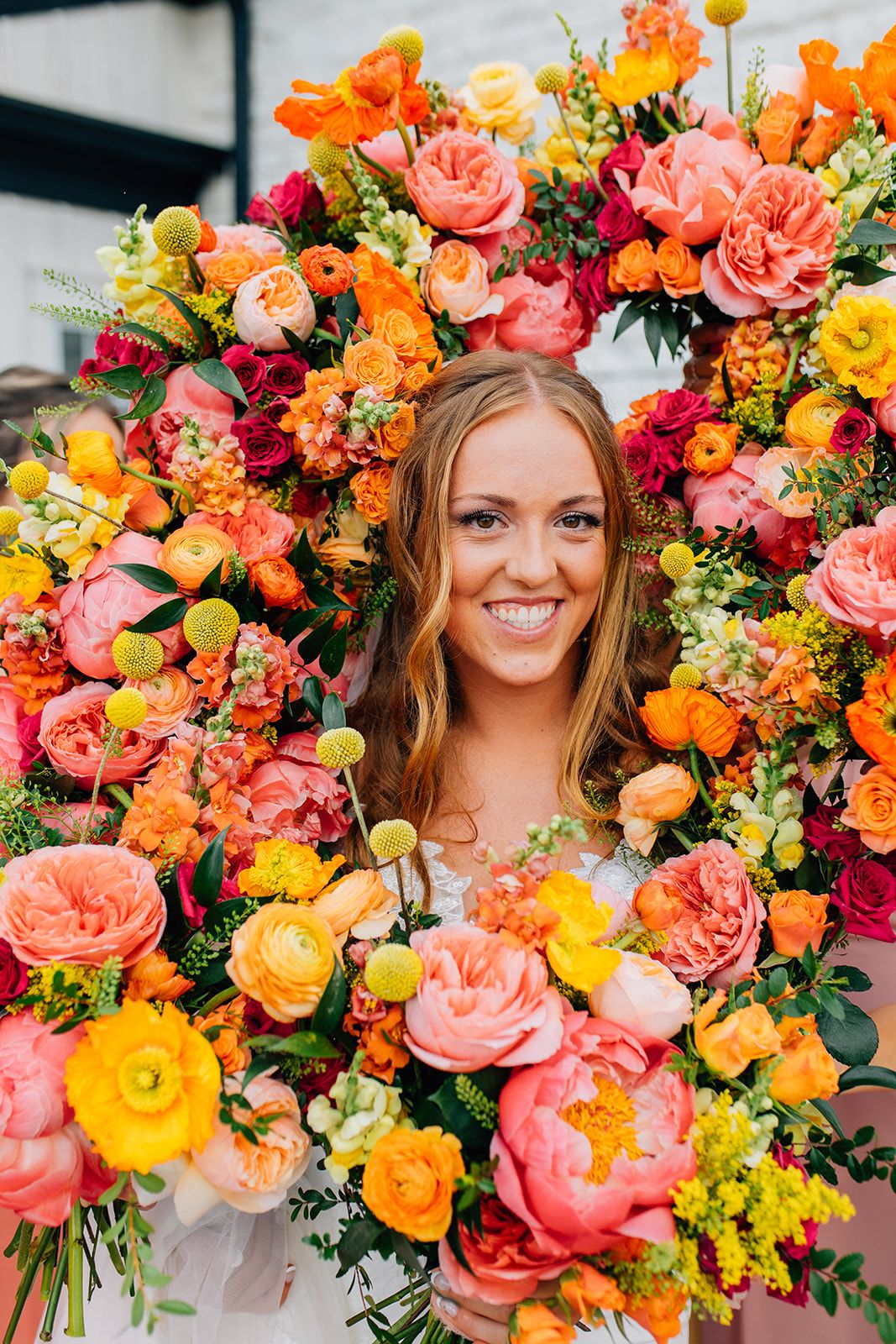 Vibrant coral and yellow flowers create a stunning floral arrangement with roses and mixed blooms in bright spring colors.