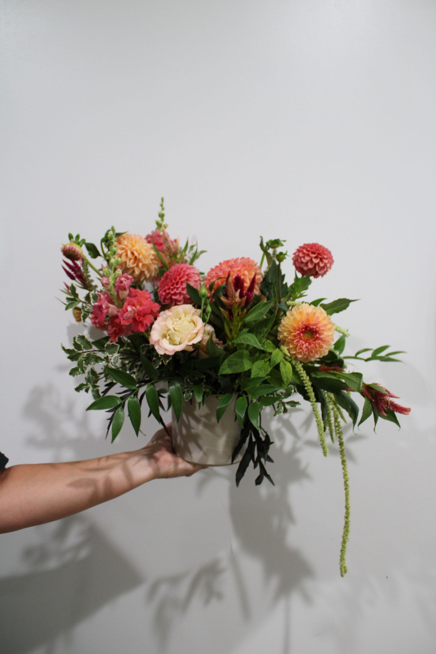 A floral arrangement featuring coral dahlias, raspberries, and greenery shown in a progression of four similar shots.
