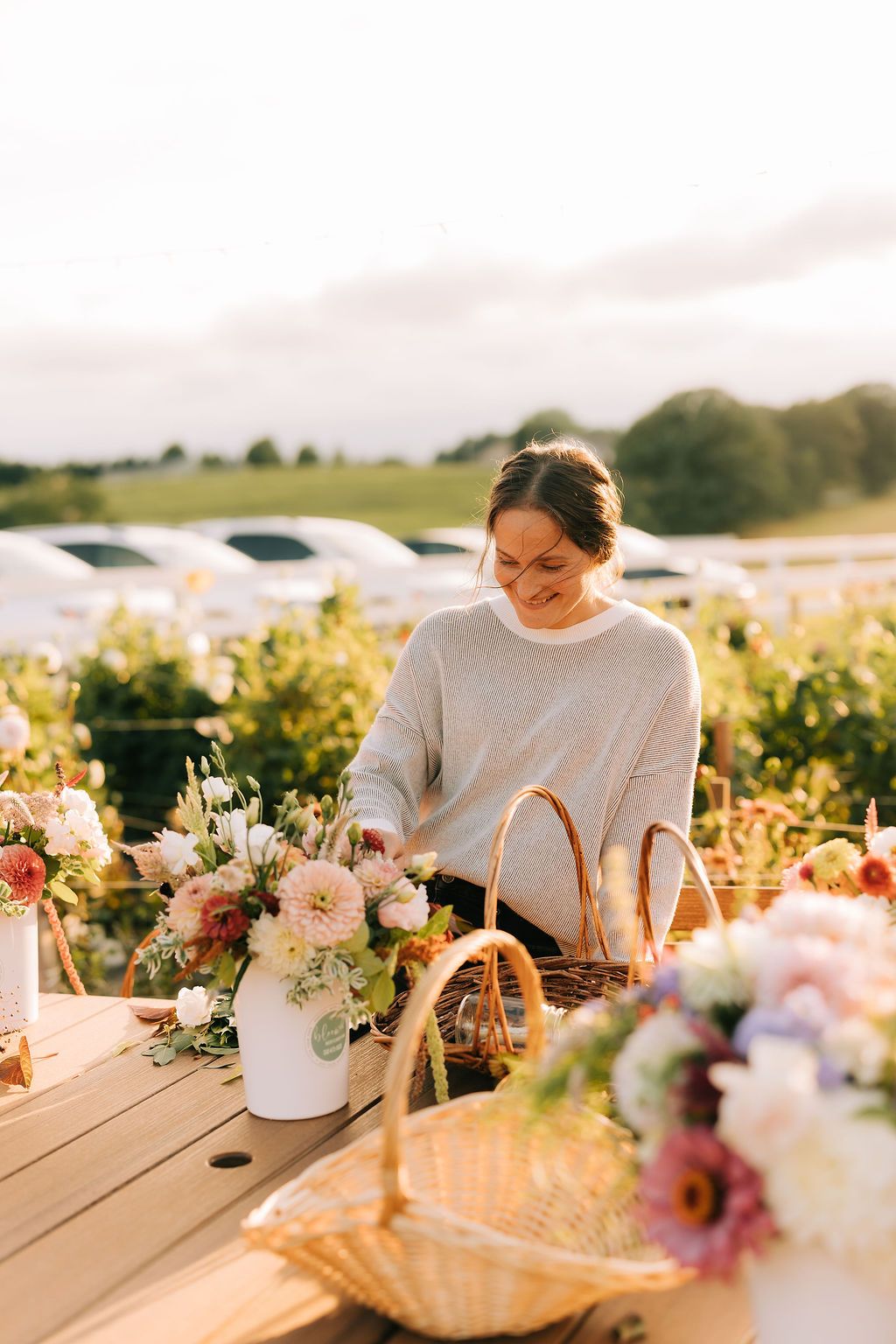 A rustic outdoor table setting at sunset with floral arrangements and place settings on a wooden deck.
