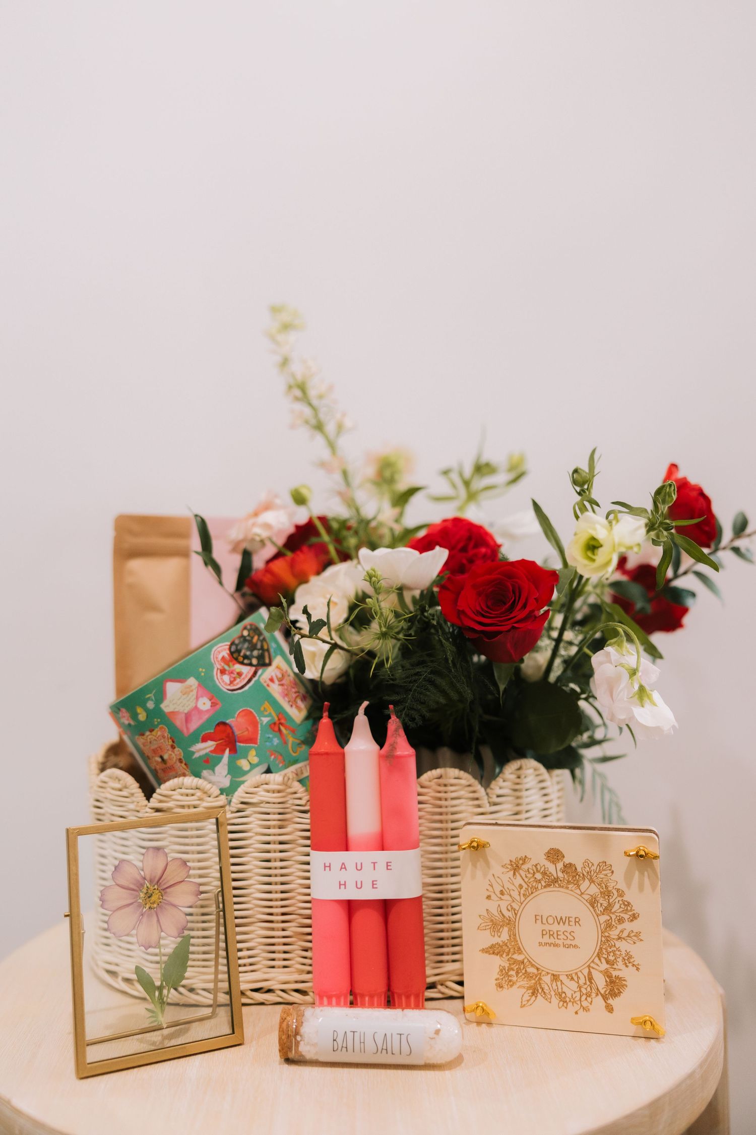 A romantic arrangement of red roses with candles, decorative frames, and gift boxes on a white table.