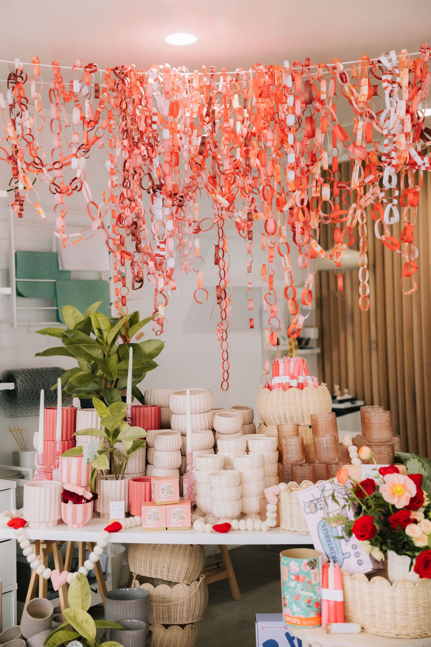 Pink paper lanterns and floral decorations hang from ceiling above elegant white party table settings with red accents.