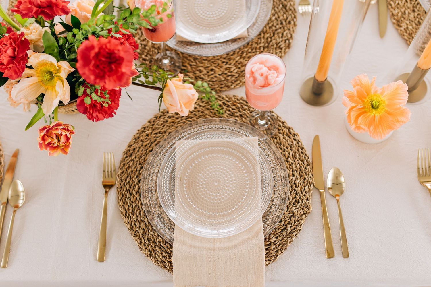 Elegant table setting with woven charger, gold flatware, and colorful floral centerpiece.