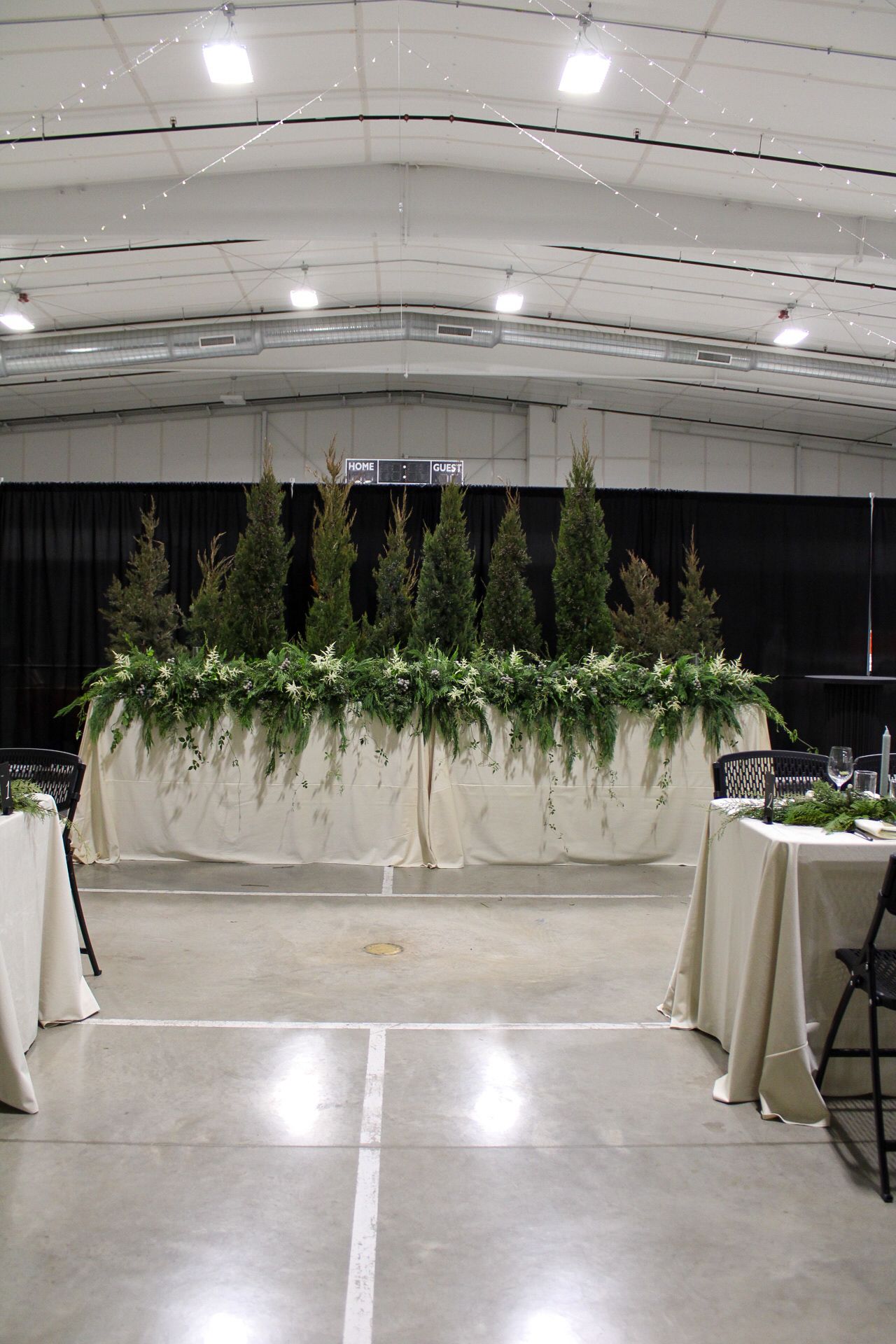 Long white draped fabric with greenery decorations hangs across an indoor event space with industrial ceiling.