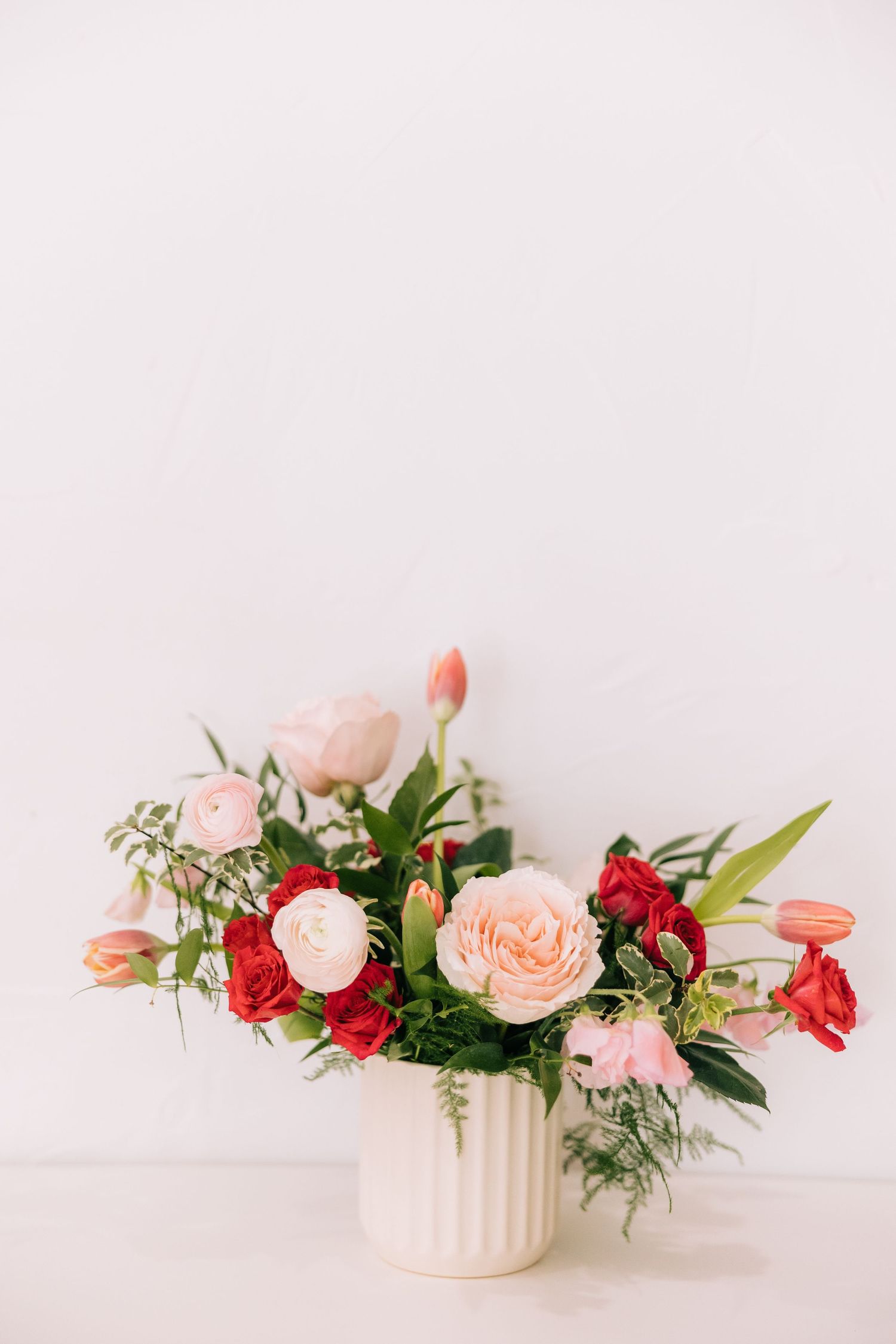 Romantic floral arrangement featuring blush roses and red flowers in a white ceramic vase.