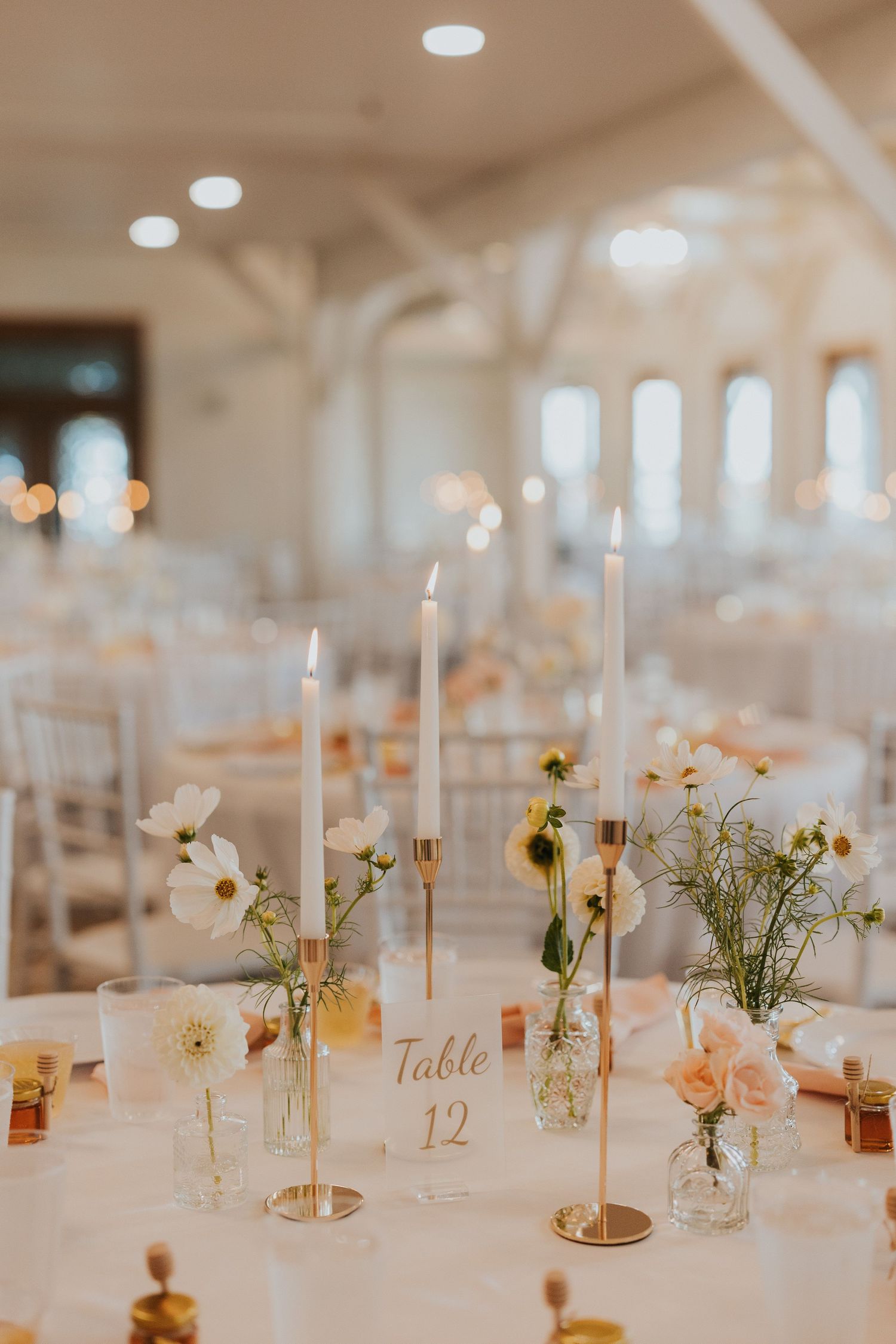 Elegant wedding reception table with white taper candles, delicate floral arrangements, and a table number card.