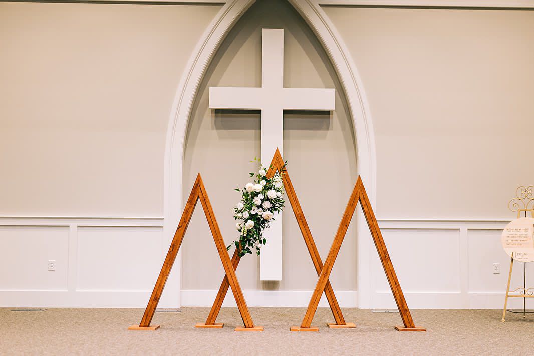 Modern wooden geometric altar design with cross and floral arrangement in church setting.