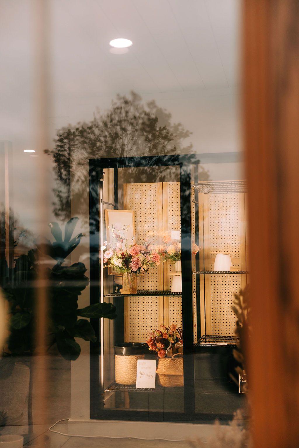 Warm glowing interior scene through window panes with decorative rattan screens and floral arrangements at dusk.