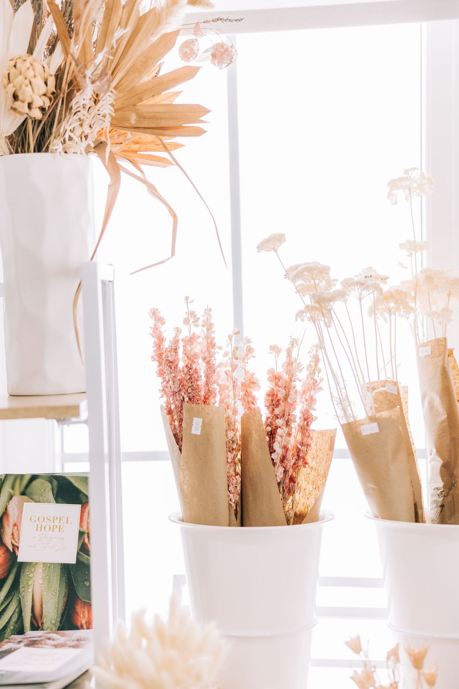 Dried flowers and pampas grass displayed in white vases near a bright window.