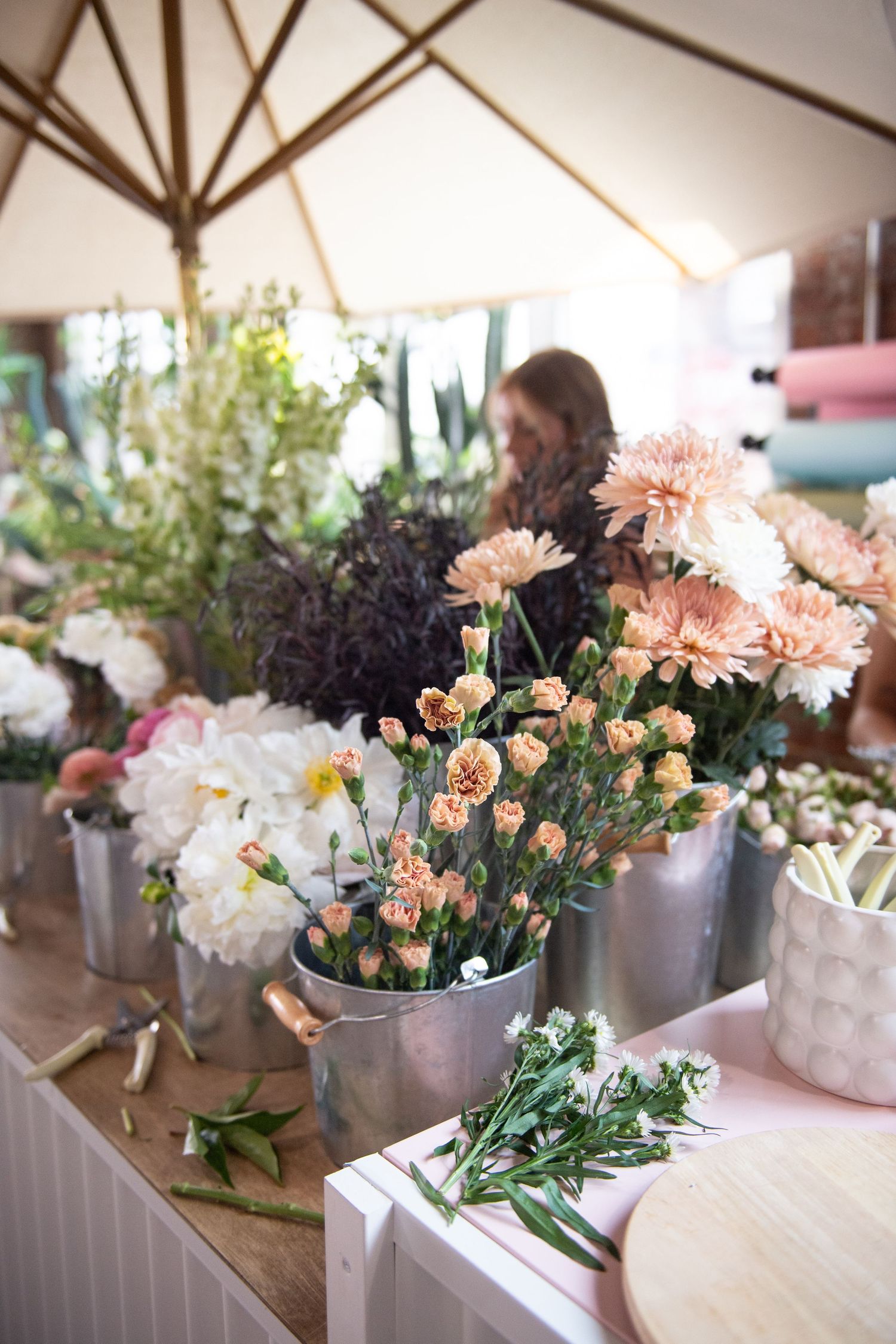 Fresh pink and white flowers arranged in metal buckets on a wooden display table at an event.