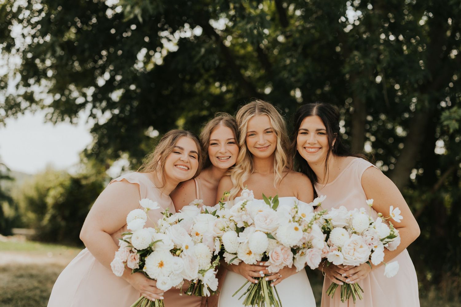 Bridal party holding white floral bouquets posing outdoors in natural lighting.
