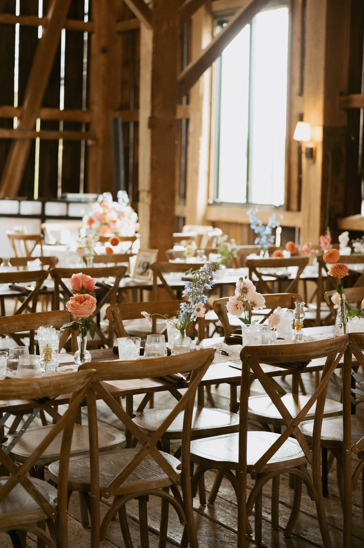 Rustic wedding reception venue with wooden cross-back chairs and long tables set for an elegant celebration.