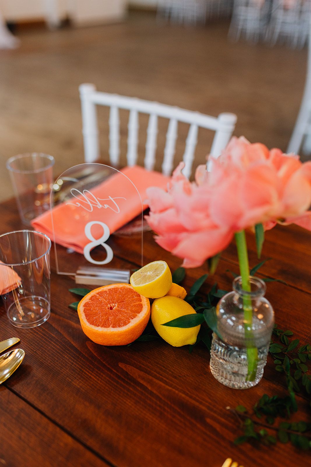 Fresh citrus fruits and pink flowers arranged on a wooden table with glassware for a brunch setting.