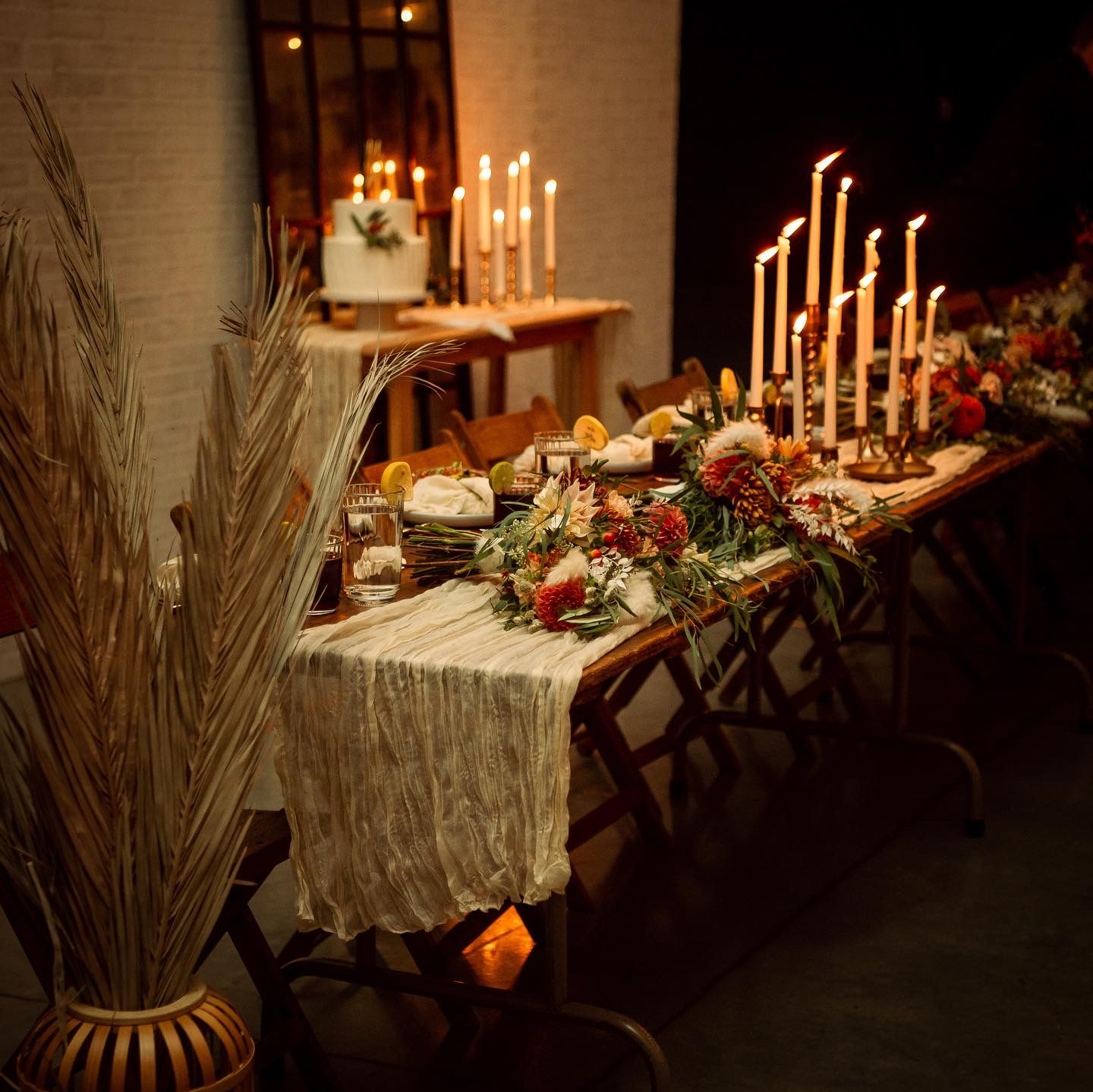 Romantic candlelit reception table with autumn floral arrangements and gold tapered candles.
