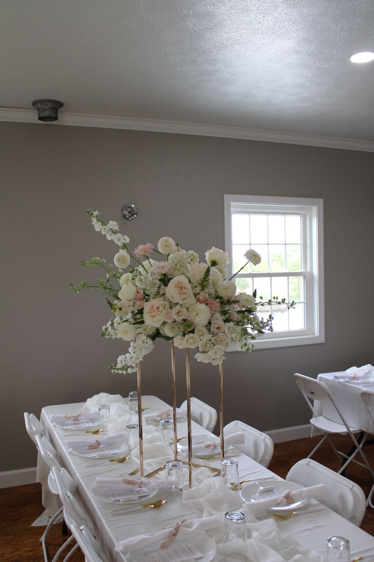 Tall white floral centerpiece arrangement on a formal table setting with natural window light.