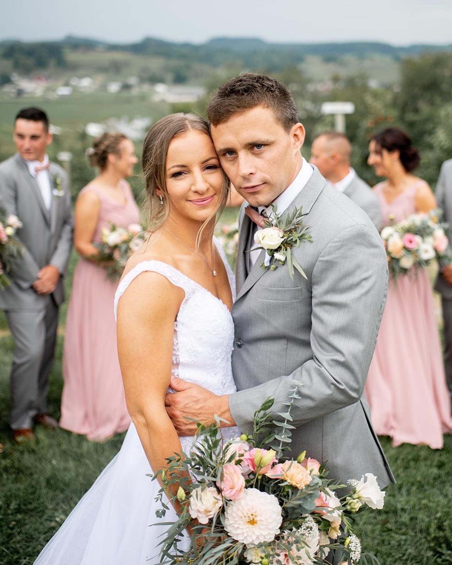 Wedding portrait with blush bridesmaid dresses and grey suit details in outdoor setting.