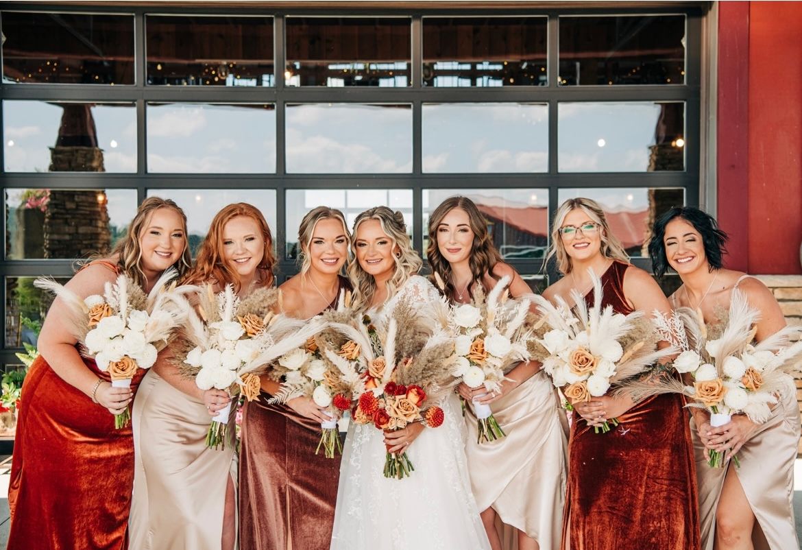 Wedding party in contrasting red and champagne dresses pose with dried floral bouquets.