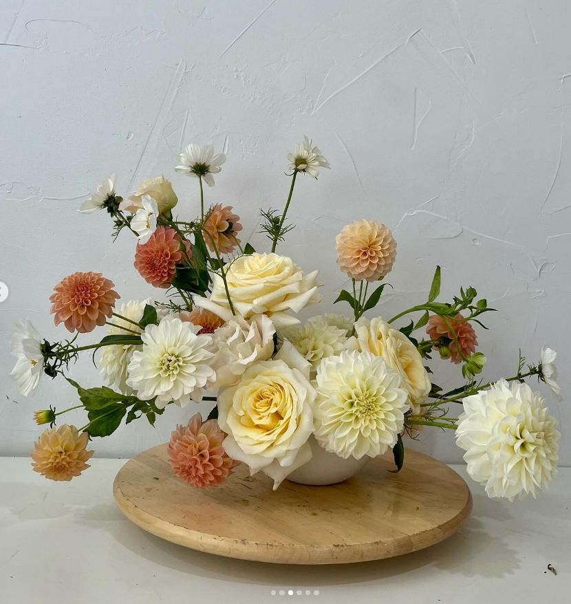 Soft peach and cream floral centerpiece featuring roses and dahlias on a wooden serving board.