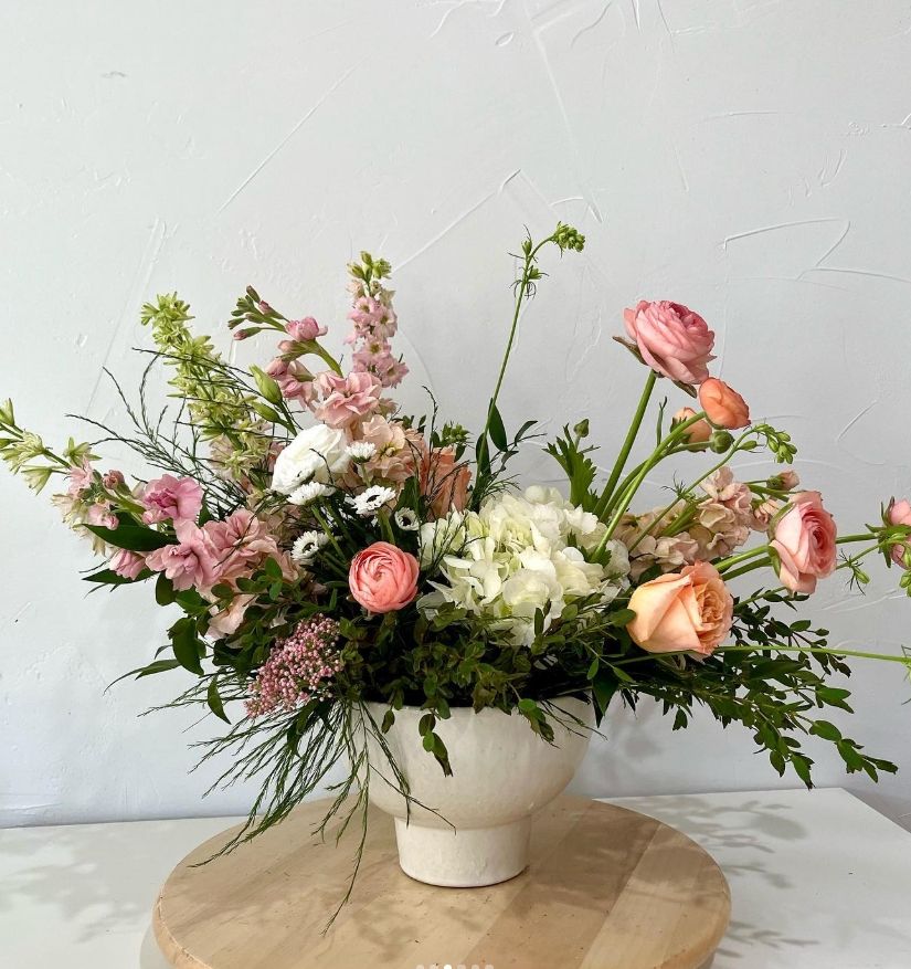 Romantic arrangement of pink and white flowers with delicate greenery in ceramic vase.