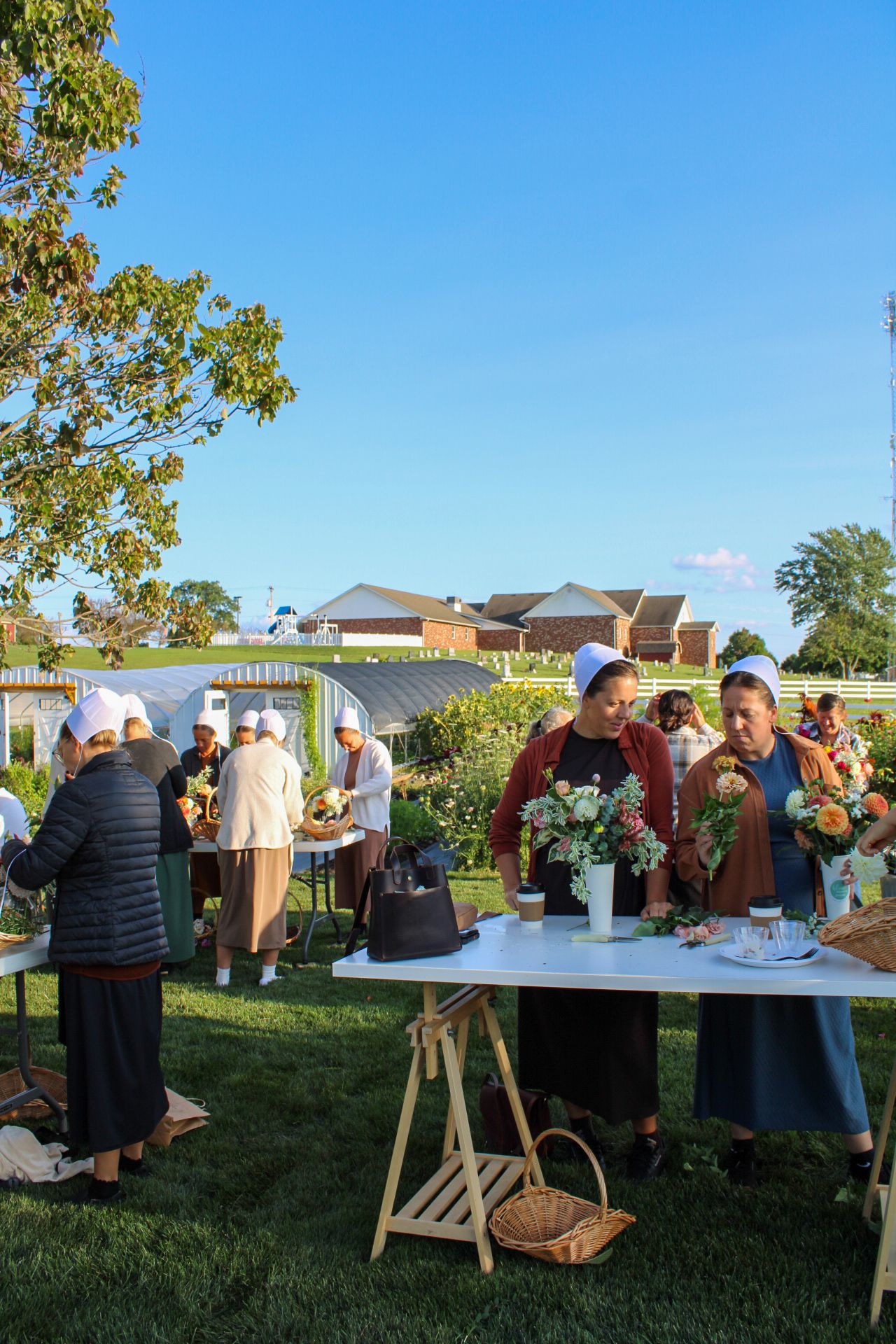 Outdoor social gathering with tables and flower arrangements under blue sky.