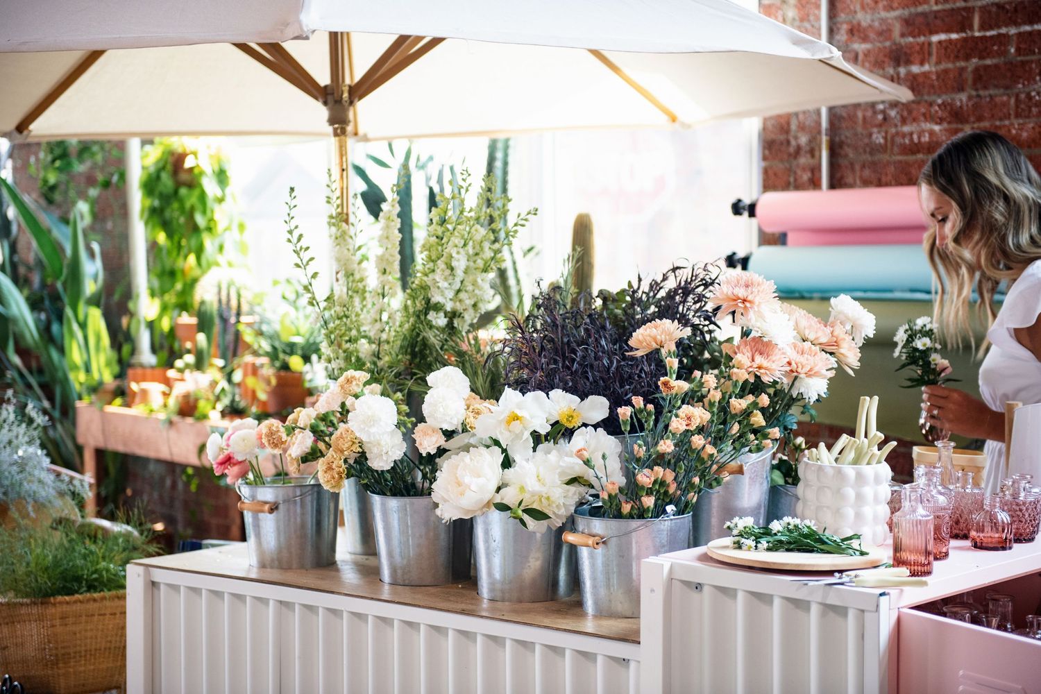 Beautiful floral display featuring white and pastel flowers in metal buckets under a market umbrella.