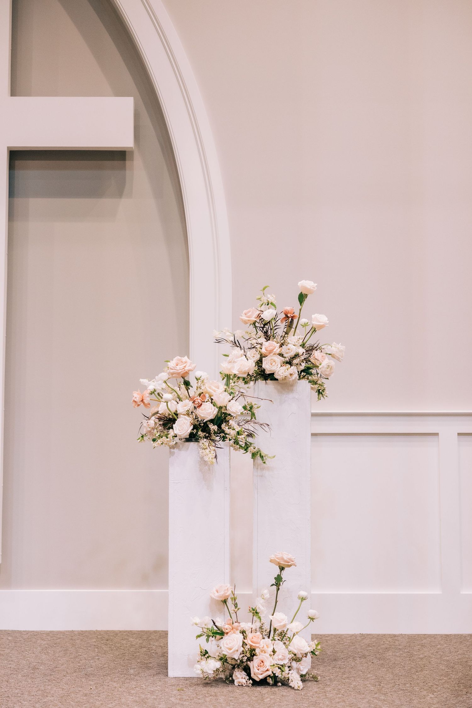 Elegant pink and white floral arrangements on white pedestals against arched wall.