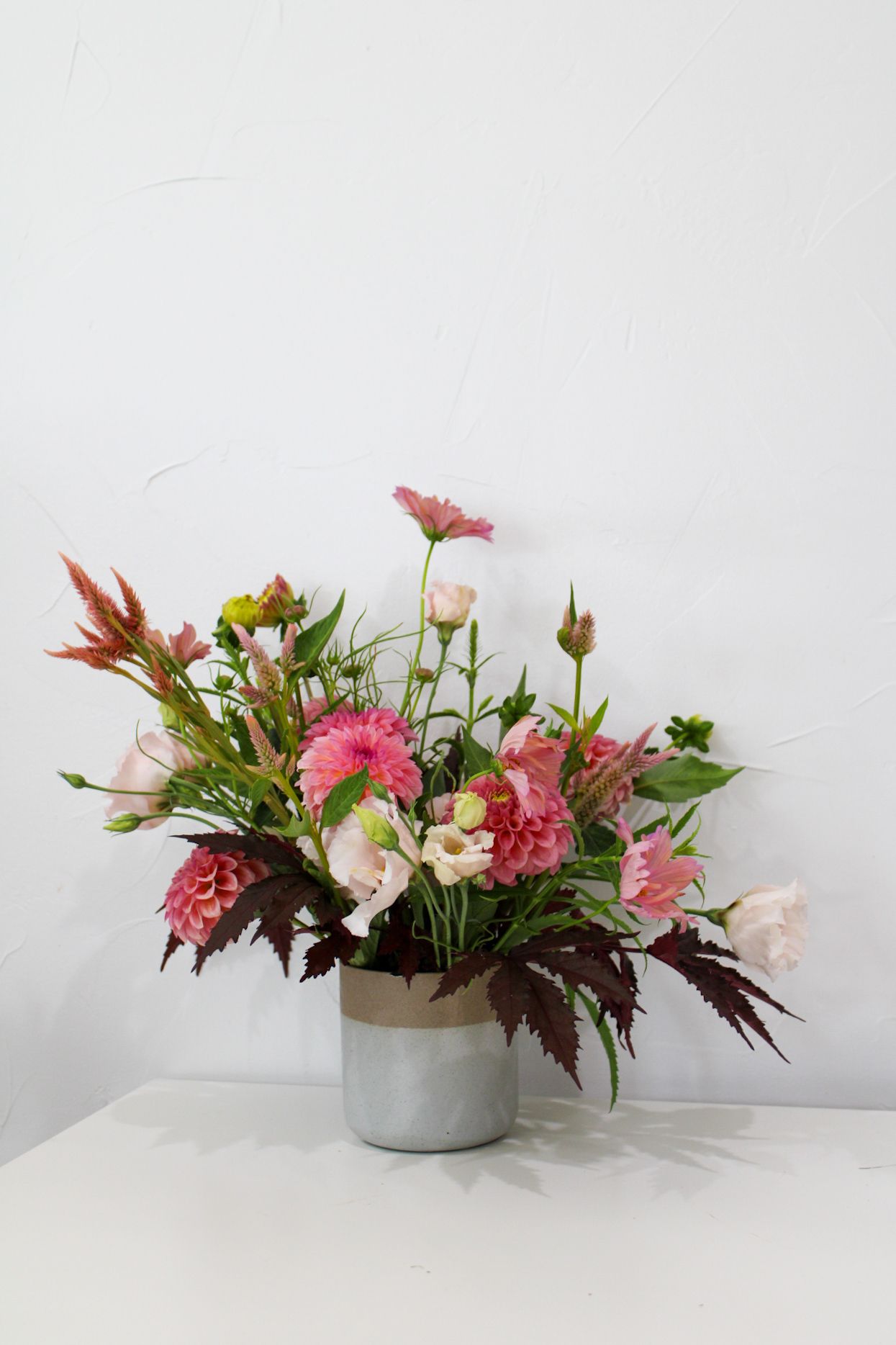 Pink and coral floral arrangement with mixed blooms in a modern concrete pot.