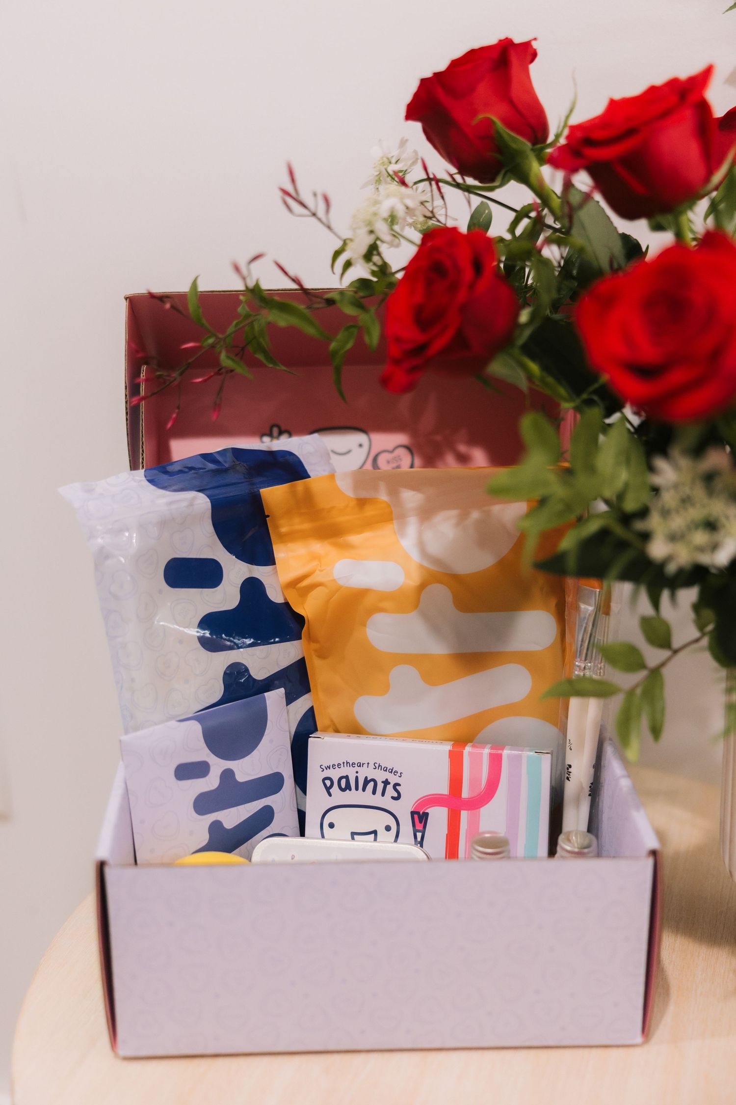 White subscription box filled with beauty products and decorated with fresh red roses on top.