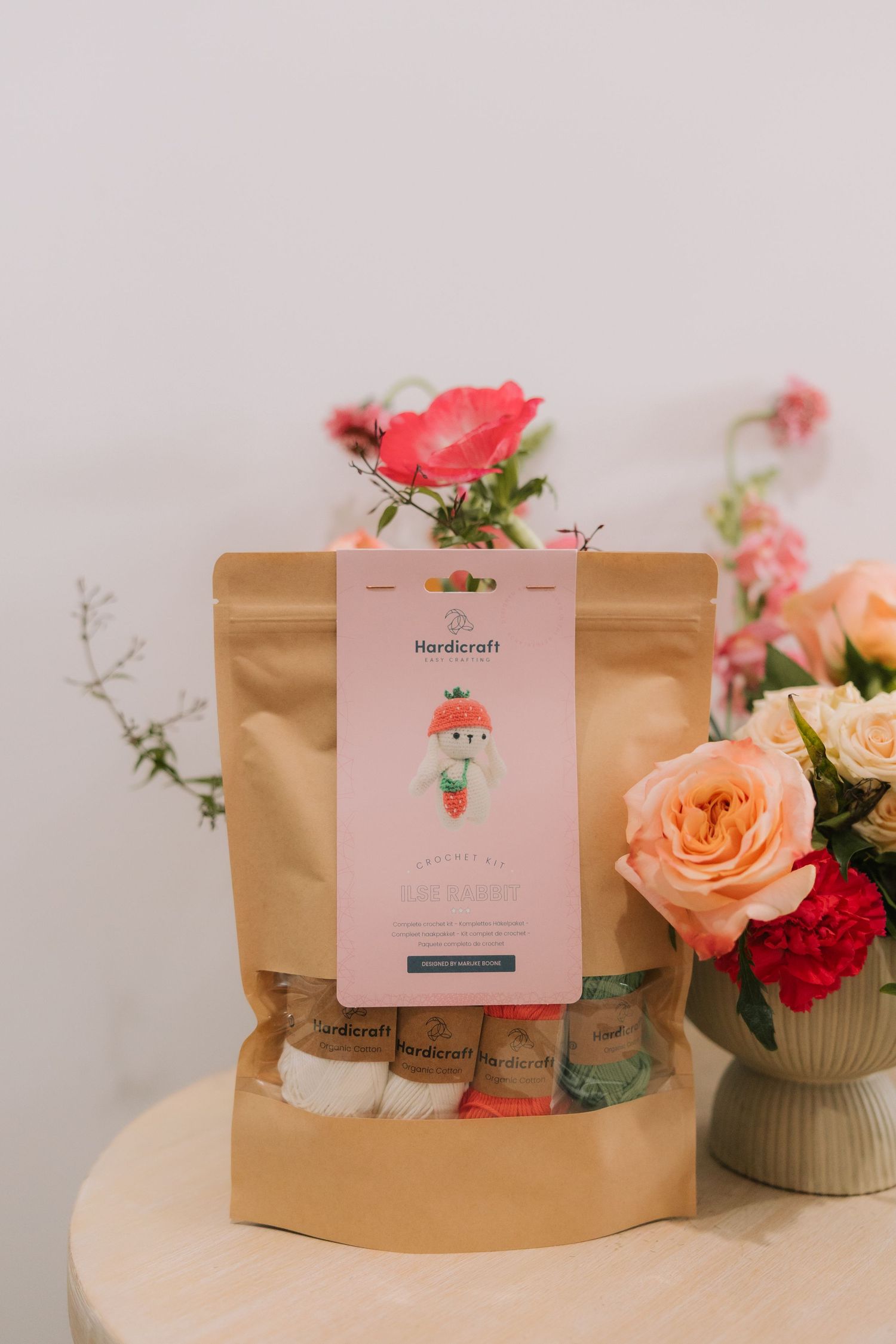 Brown paper coffee bags with pink floral cards displayed alongside peach and red roses in a minimalist setting.