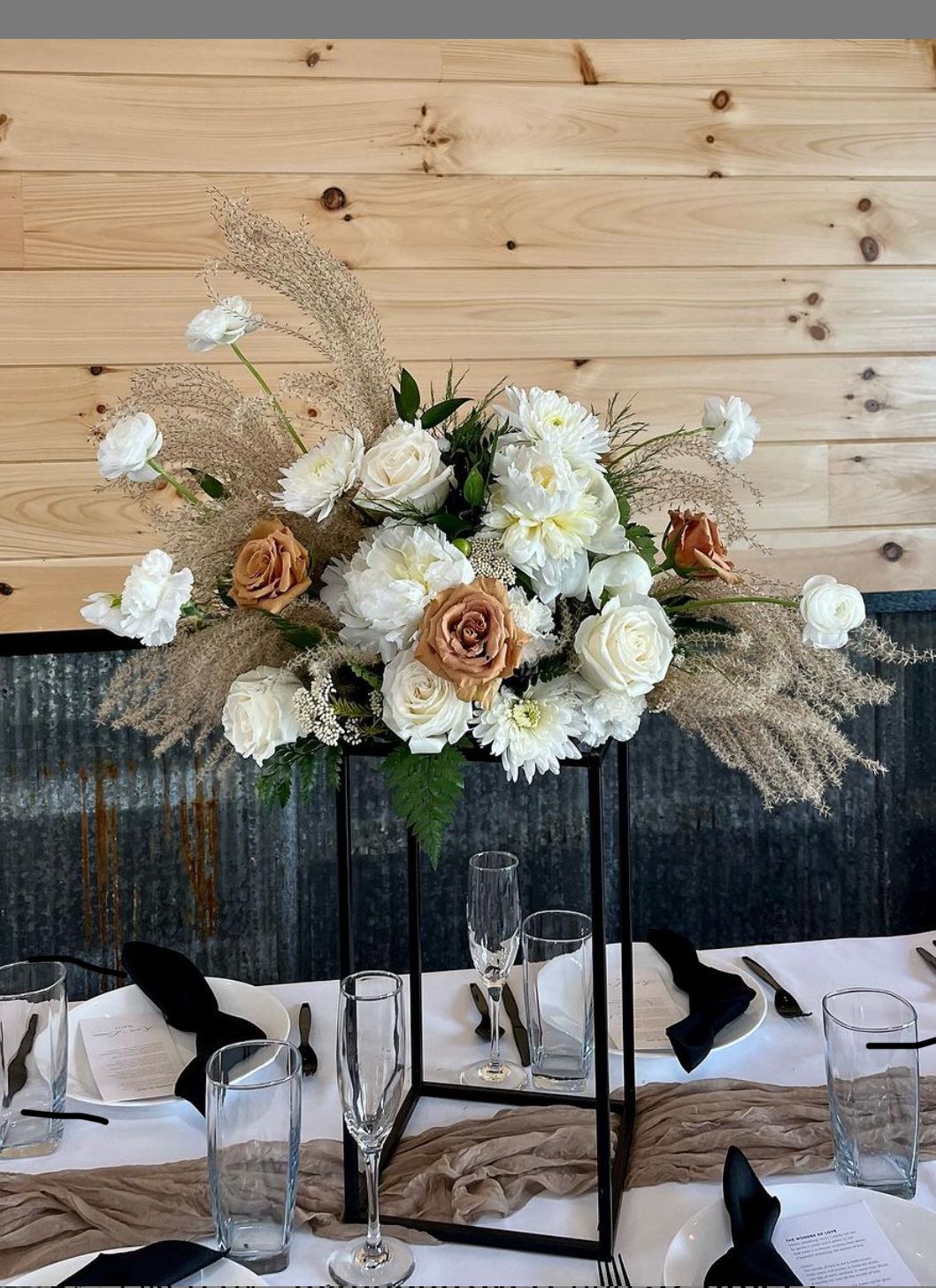 Romantic white and beige floral arrangement with dried pampas grass on dark table setting.