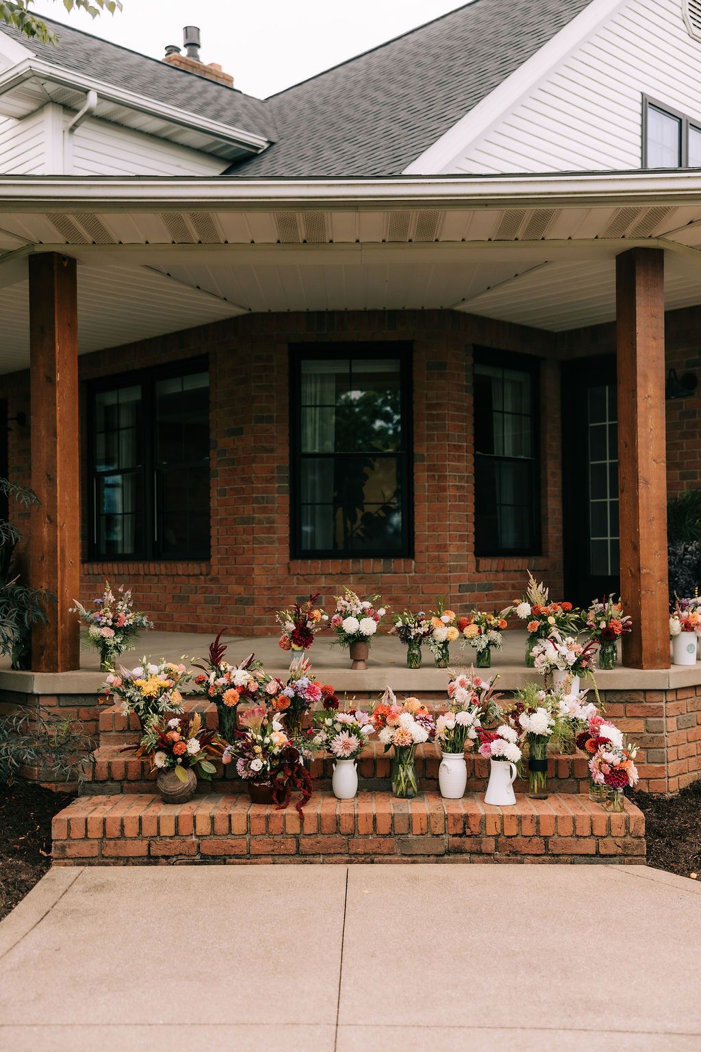 Beautiful floral arrangements in pink, white and peach colors line a brick ledge outside a residential home.