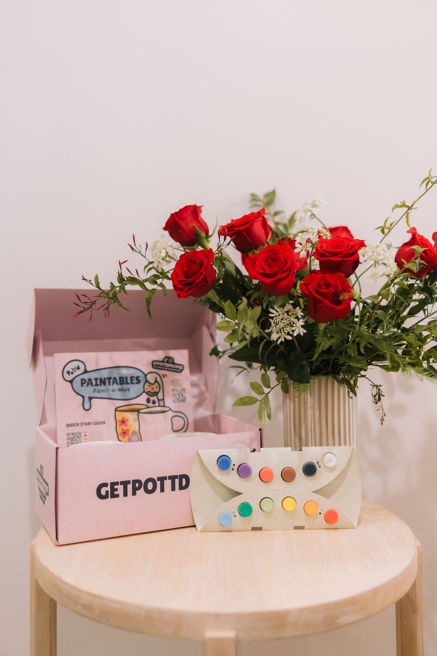 A watercolor paint set with red roses decorating a round wooden table creates an artistic still life scene.