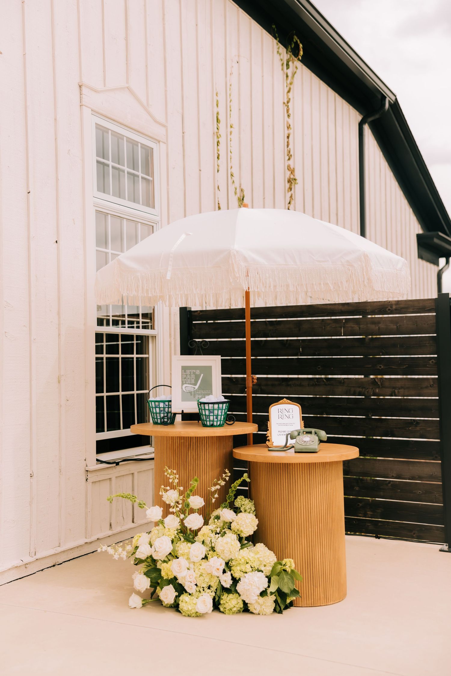 Modern white barn wedding venue interior with dark wood accent wall and elegant floral arrangements on display tables.