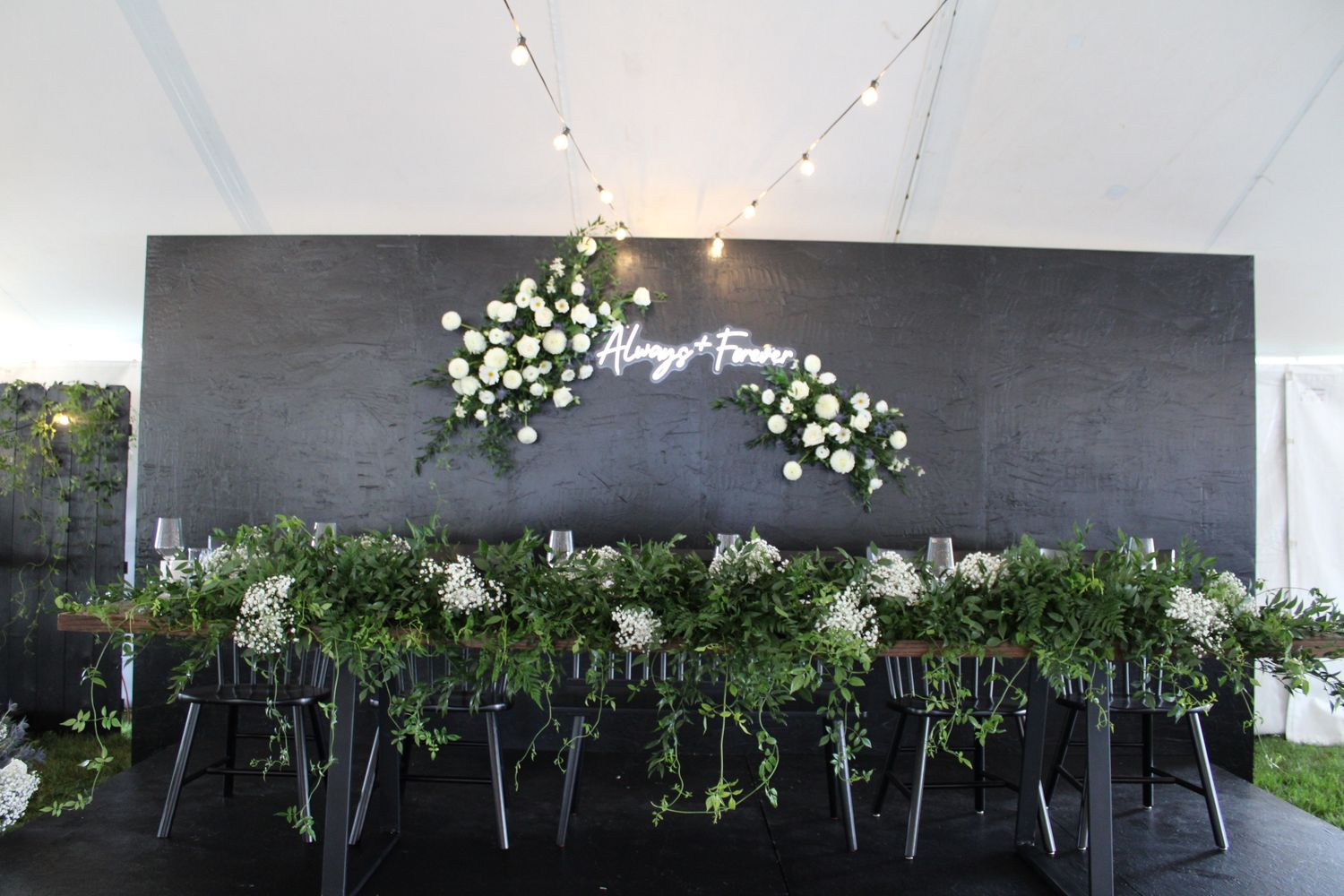 Modern black accent wall decorated with white floral arrangements and greenery for an event.
