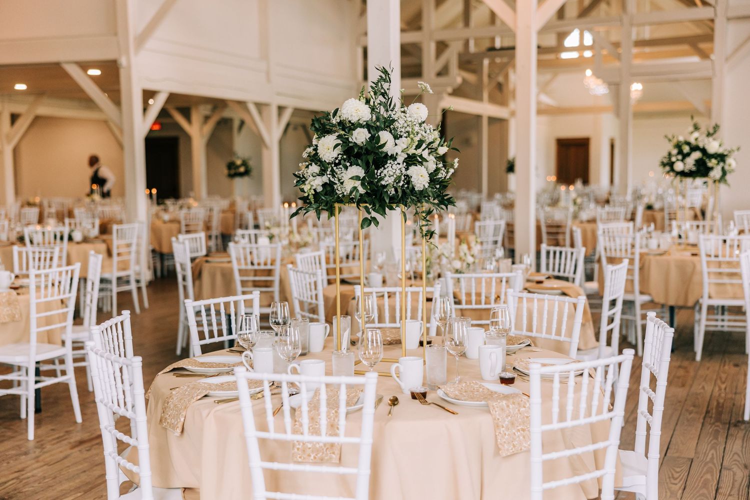 White Chiavari chairs surround round tables with tall floral centerpieces in an airy reception hall.