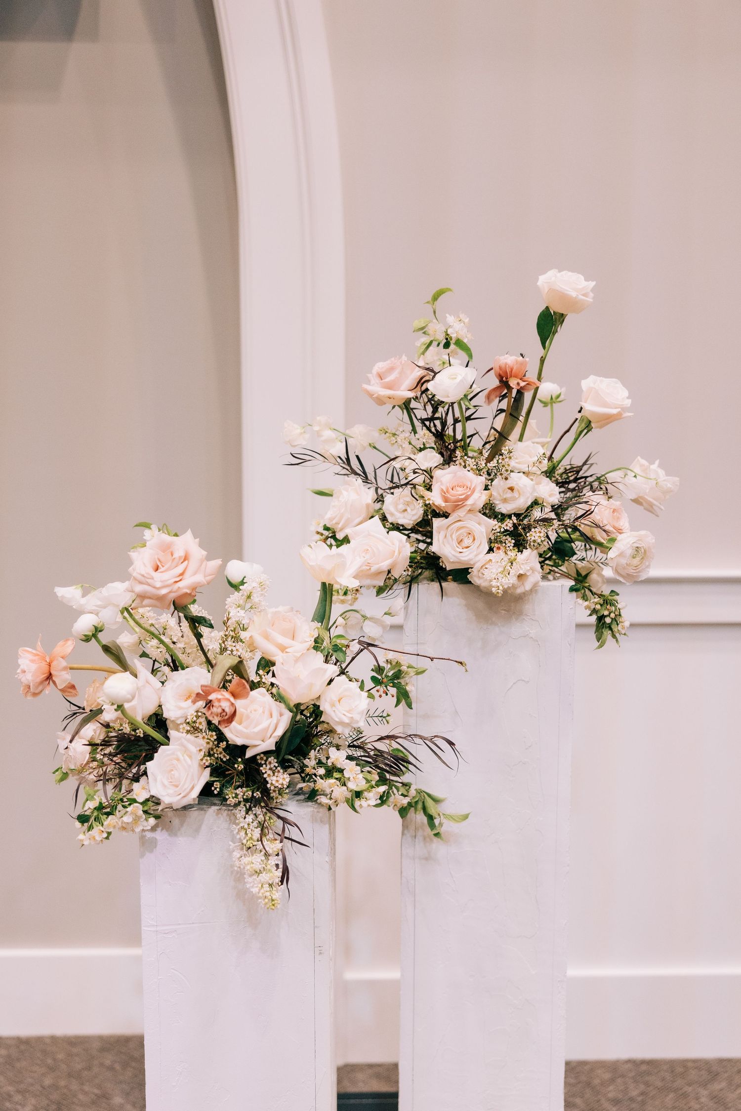 Blush pink and white flower arrangements in white modern vases against neutral wall.