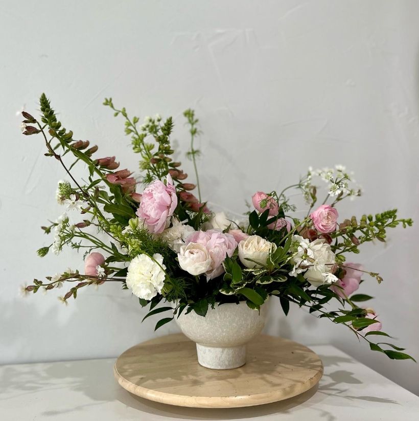 Elegant pink and white rose arrangement with delicate greenery in white ceramic vessel.