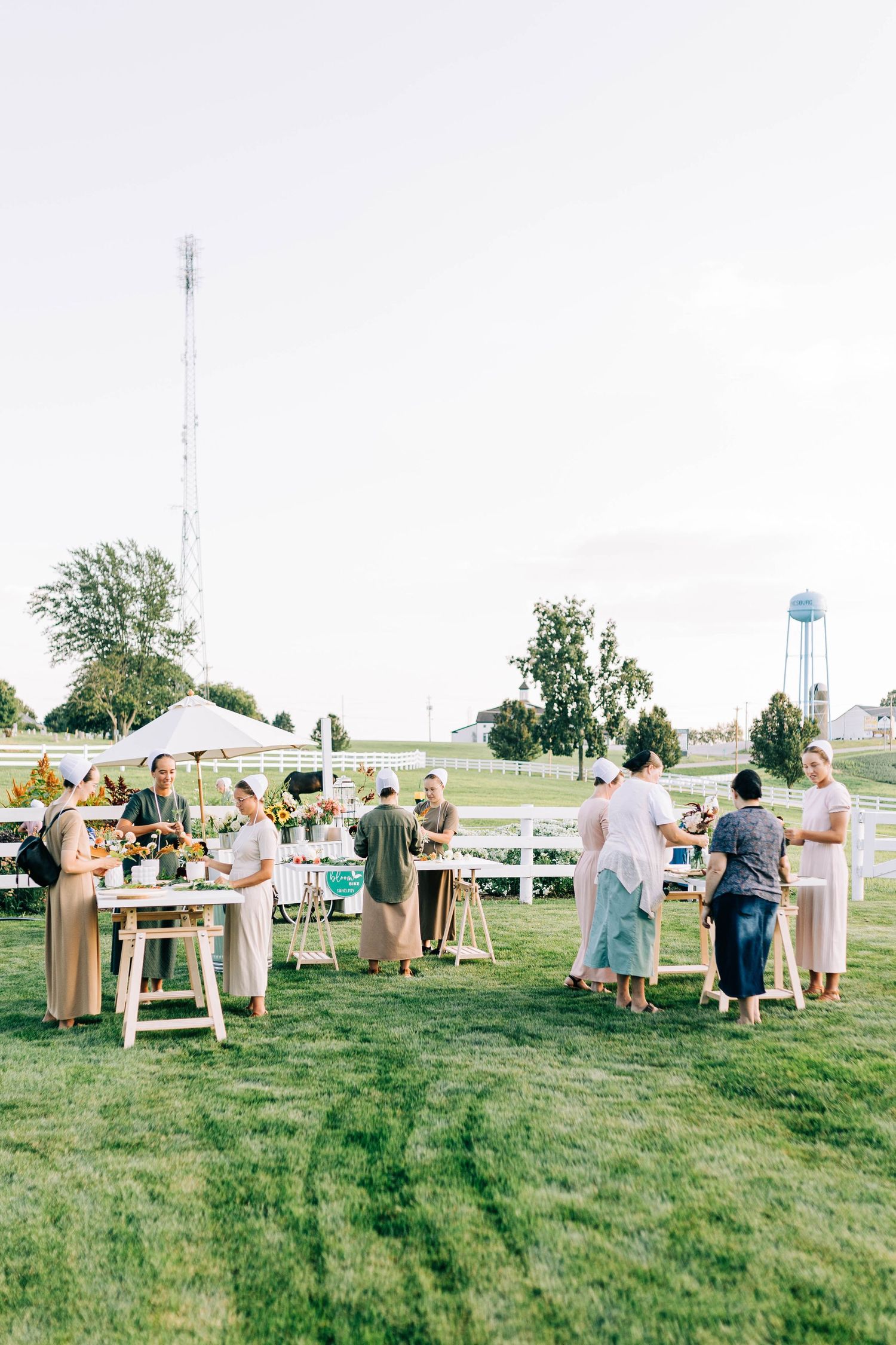 Guests gather at outdoor tables for a rustic garden party with a water tower visible in the background.