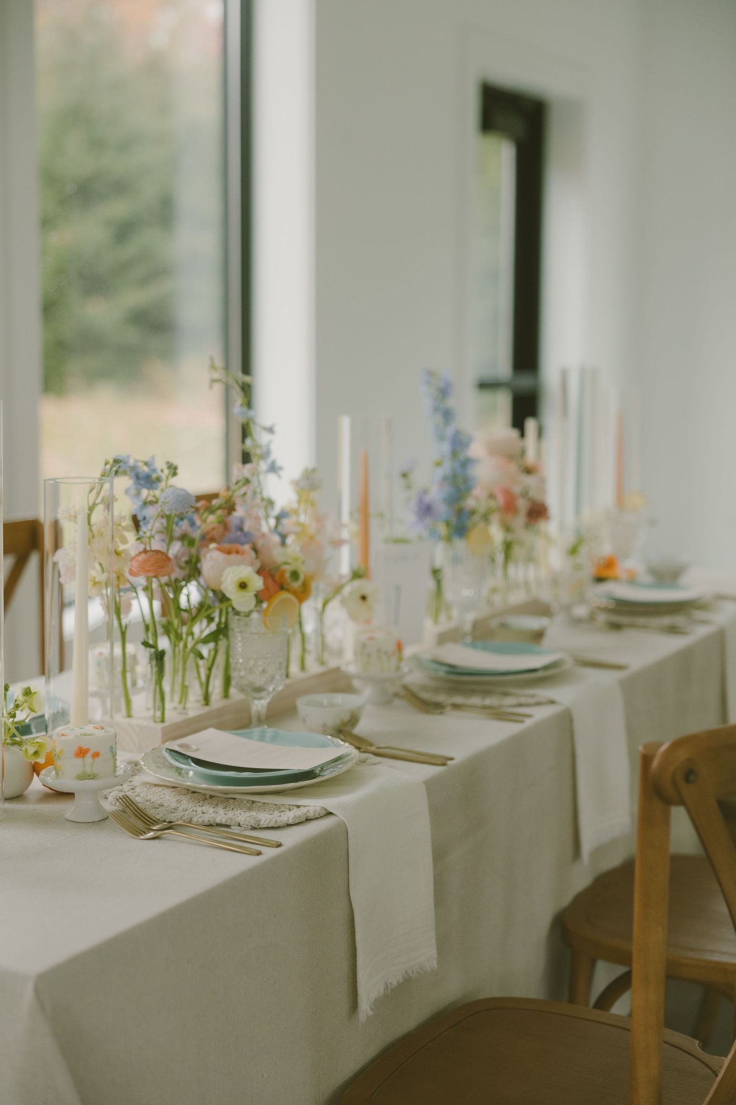Romantic table setting with white candles and delicate spring flowers in glass vases on a white tablecloth.