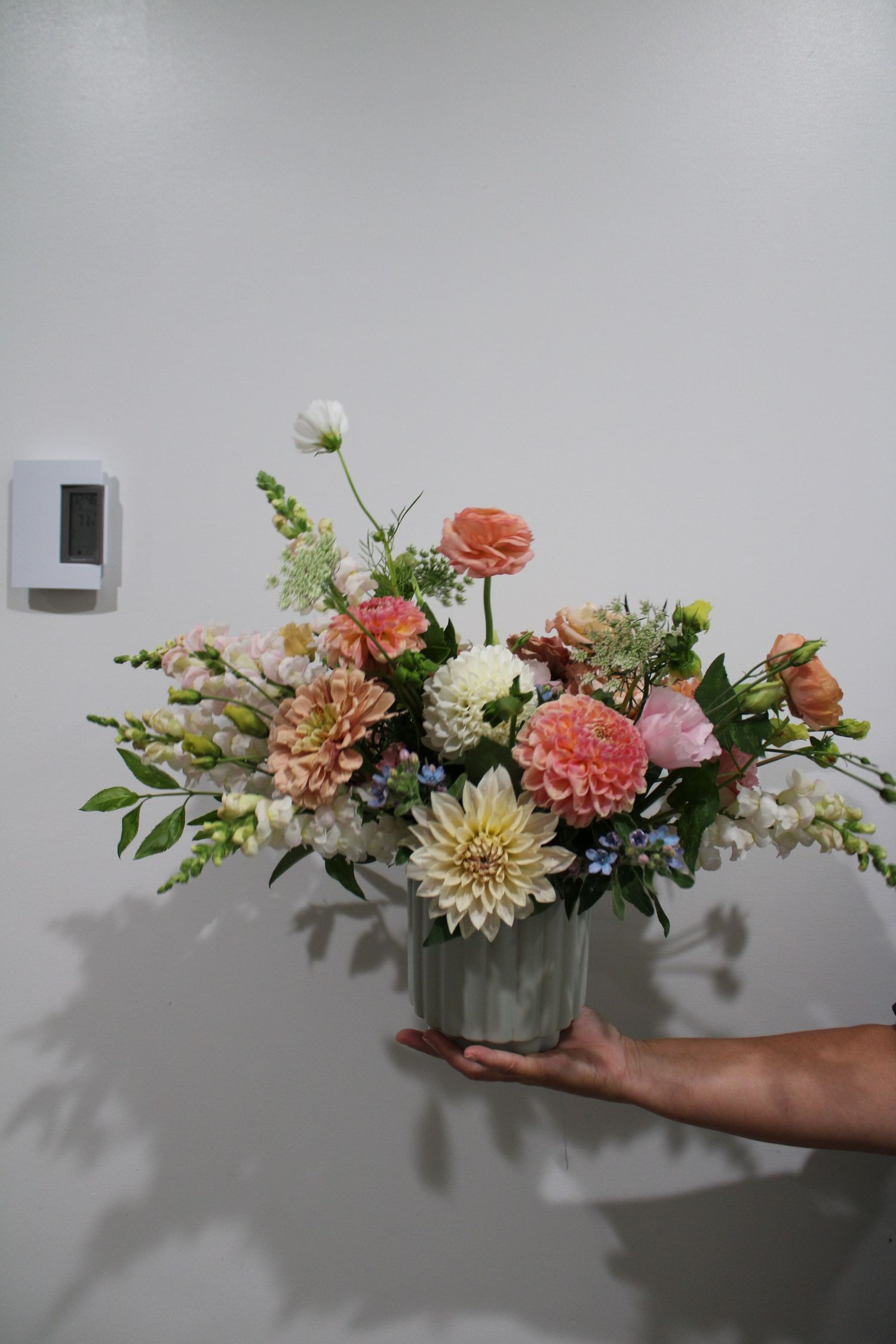 Time-lapse sequence showing floral arrangement with pink and peach dahlias being styled against a white wall.