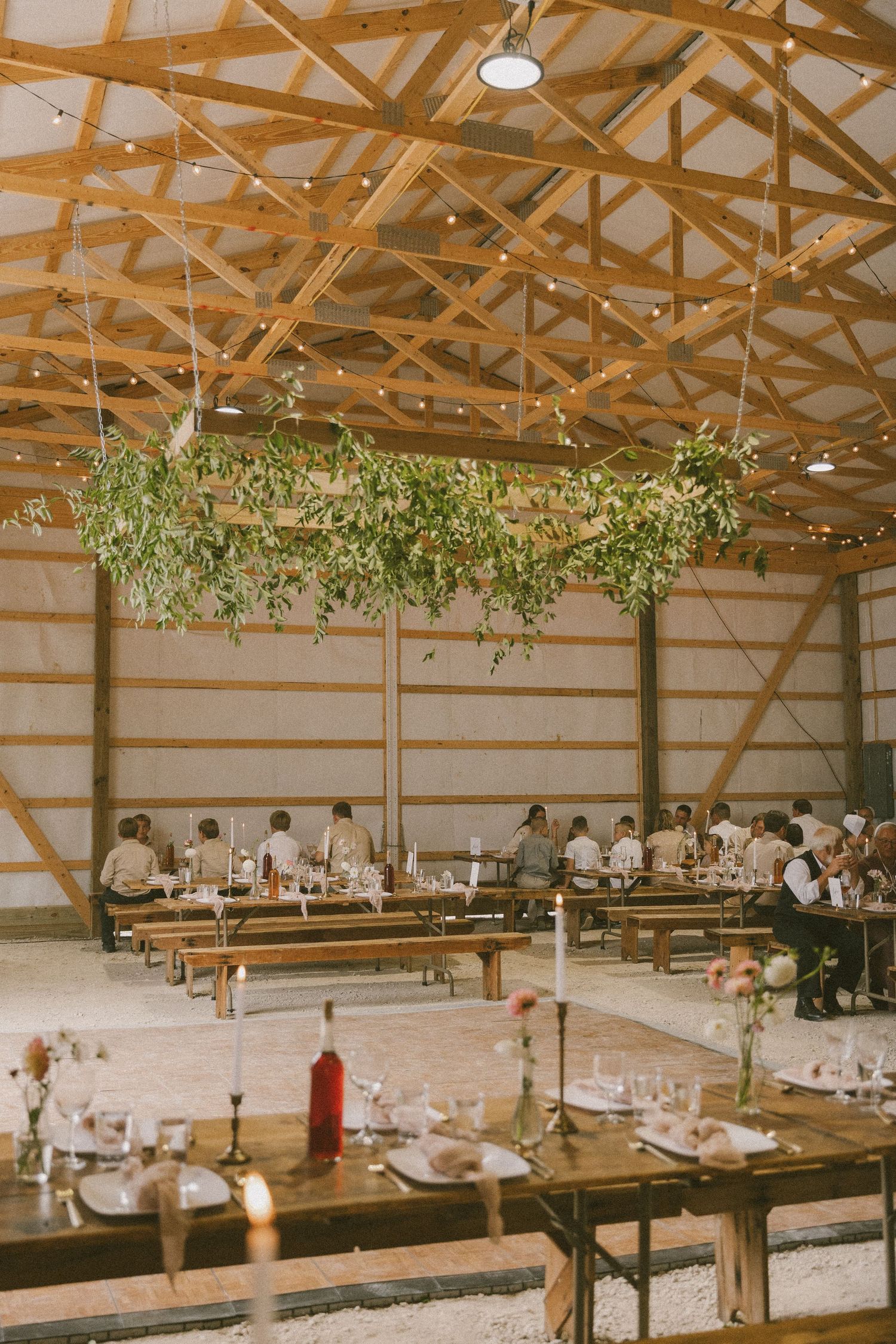 Rustic barn venue with wooden beams and hanging greenery over long wooden dining tables.