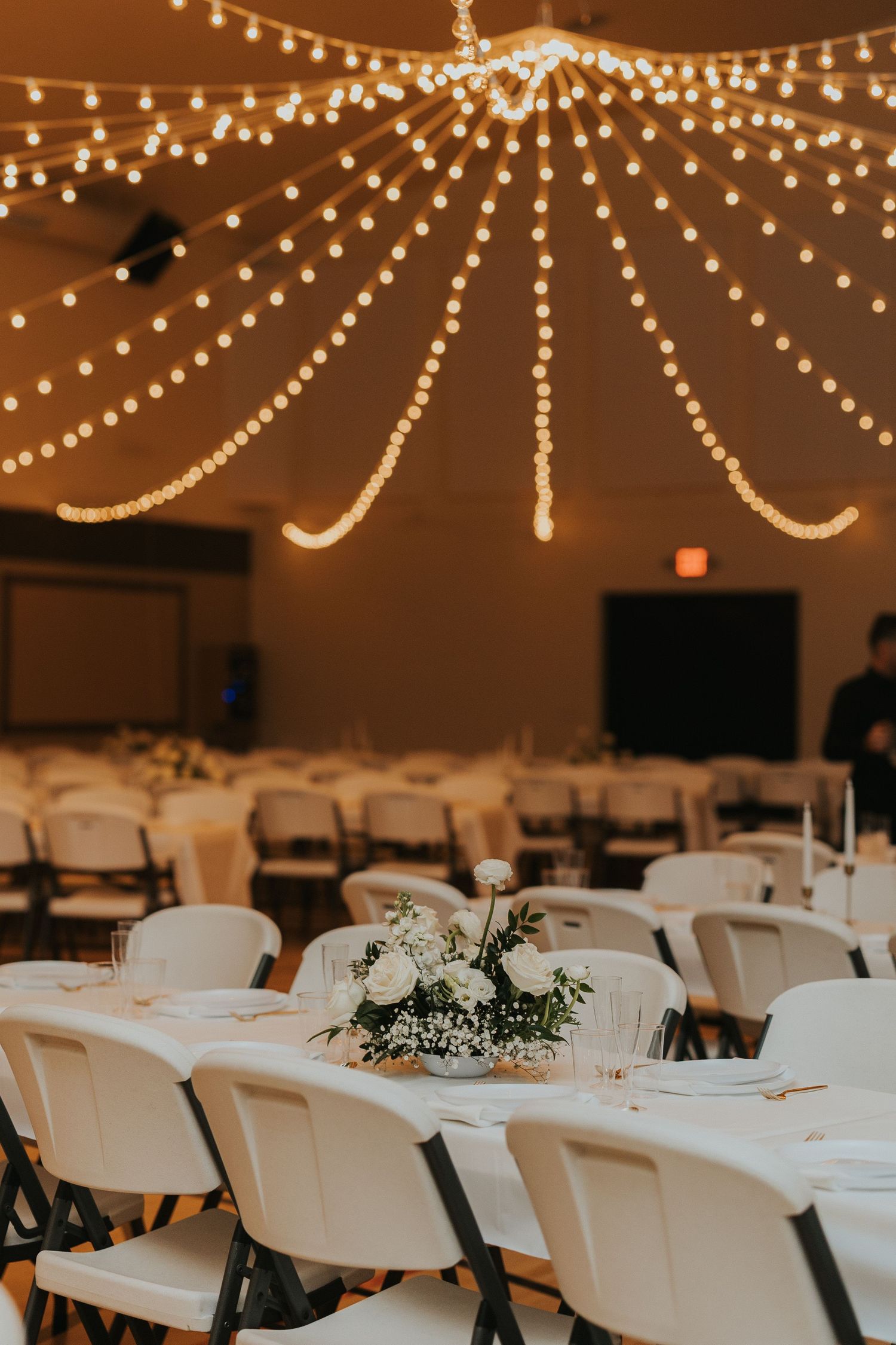 Wedding reception venue decorated with string lights and white tables adorned with floral centerpieces.