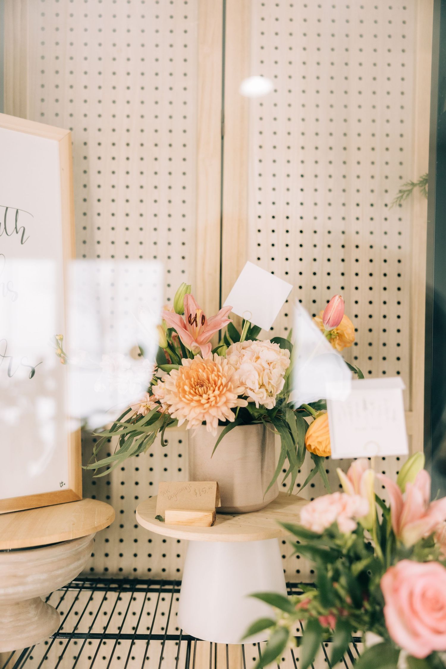 Delicate floral arrangement with pink and peach blooms displayed against a white pegboard wall.