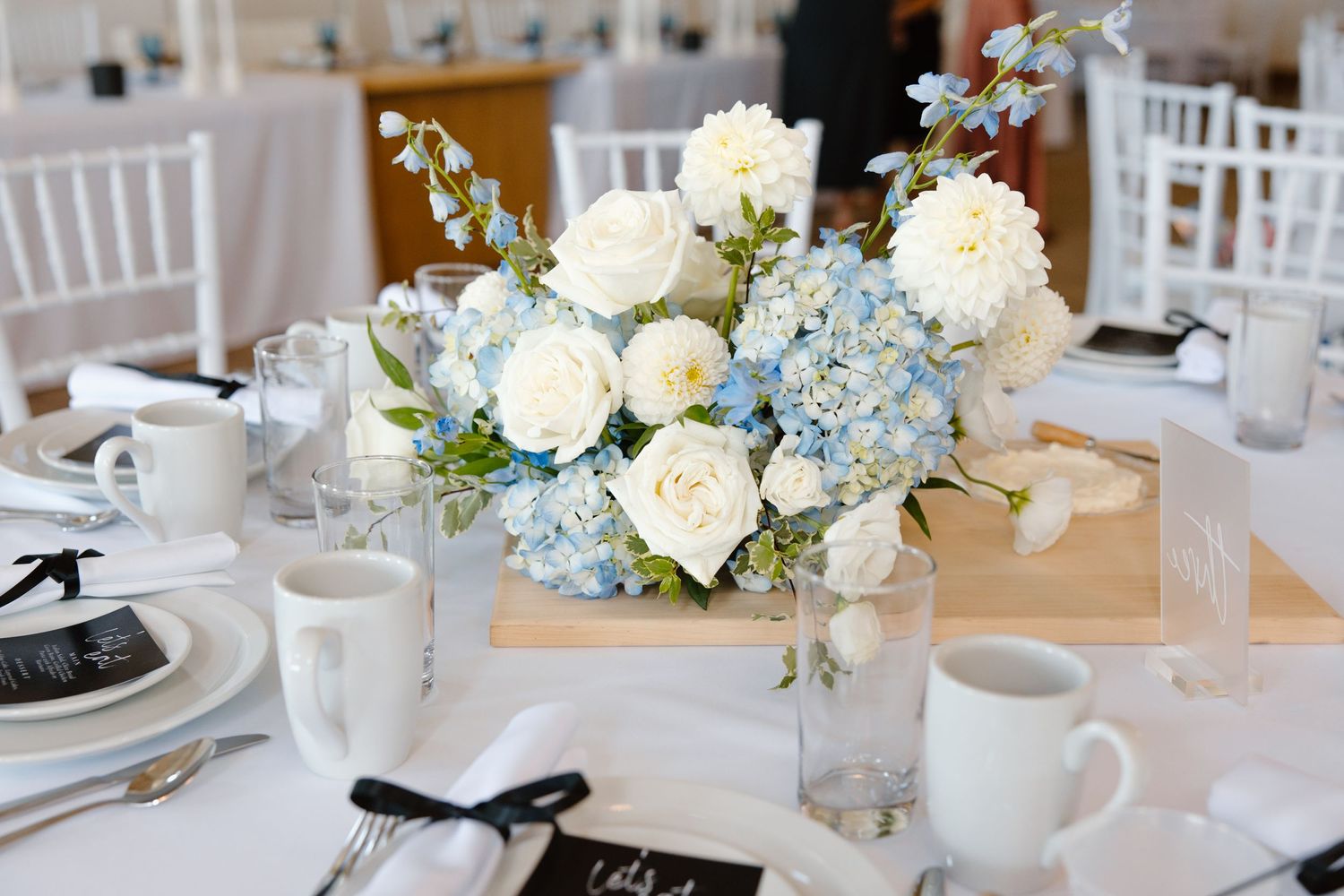 Blue and white floral centerpiece with roses and hydrangeas on white tablecloth.