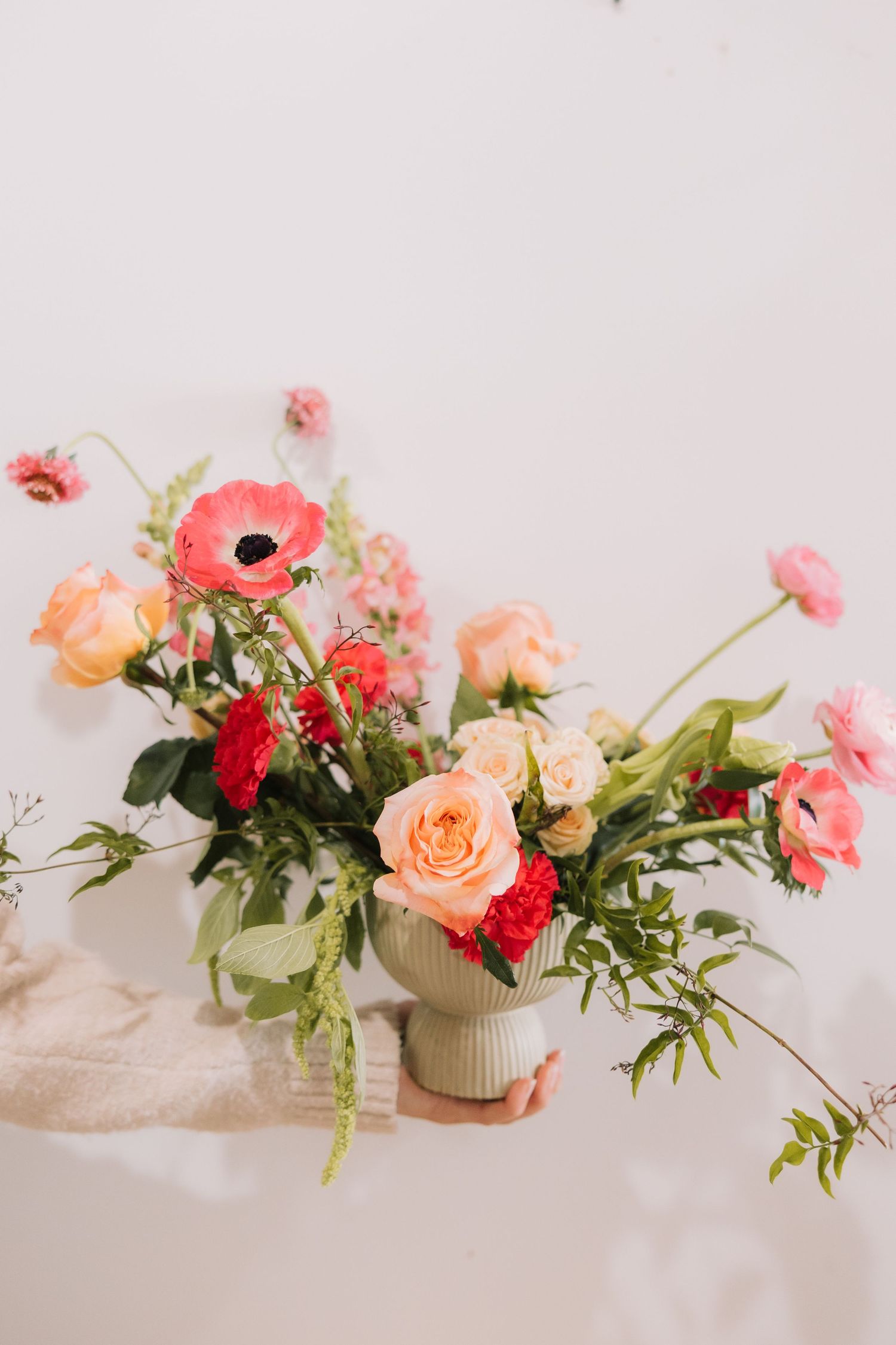 Delicate pink and peach flowers with greenery arranged in small white ceramic vases on a light neutral surface.