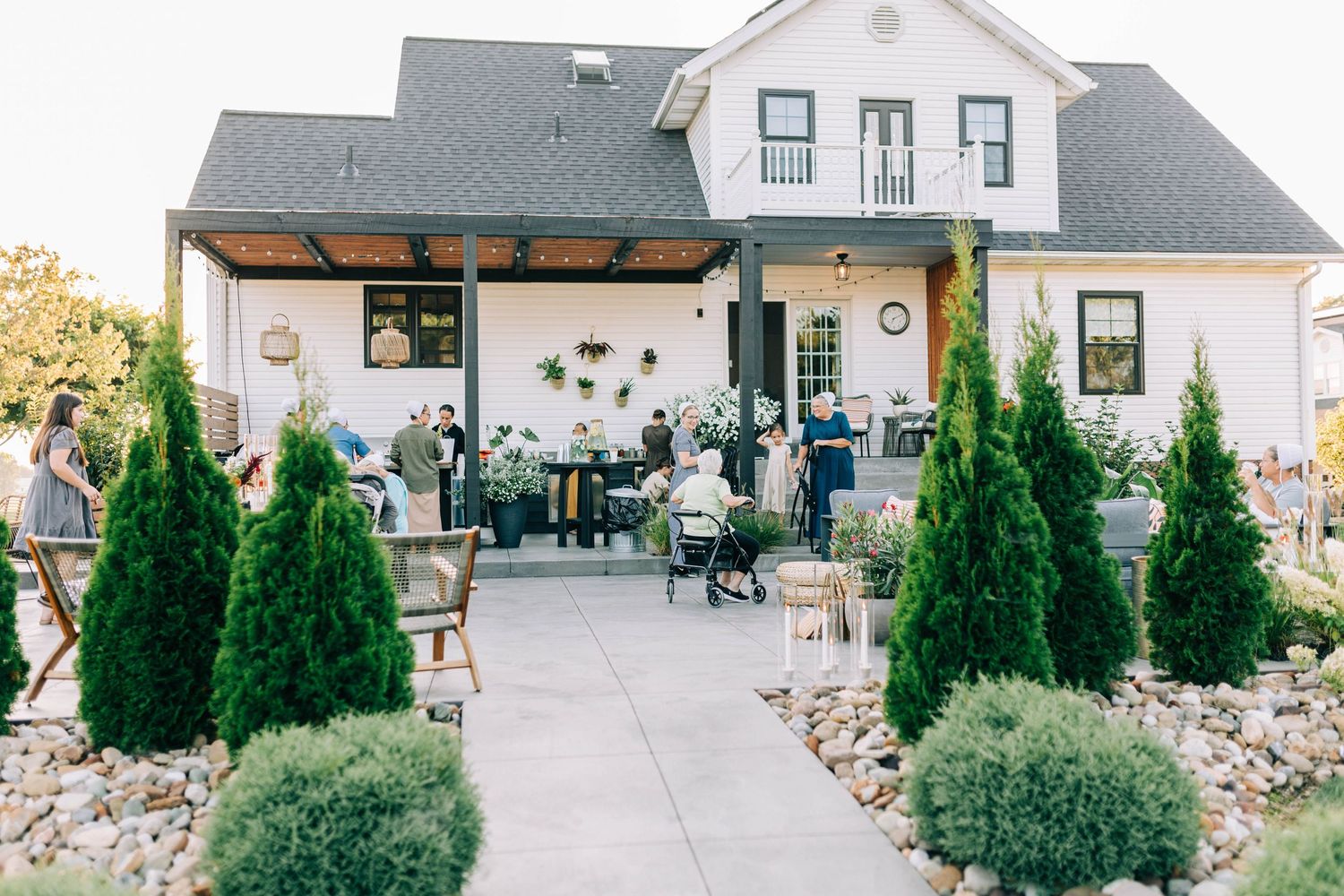 White farmhouse-style building with cypress trees and landscaped garden entrance.