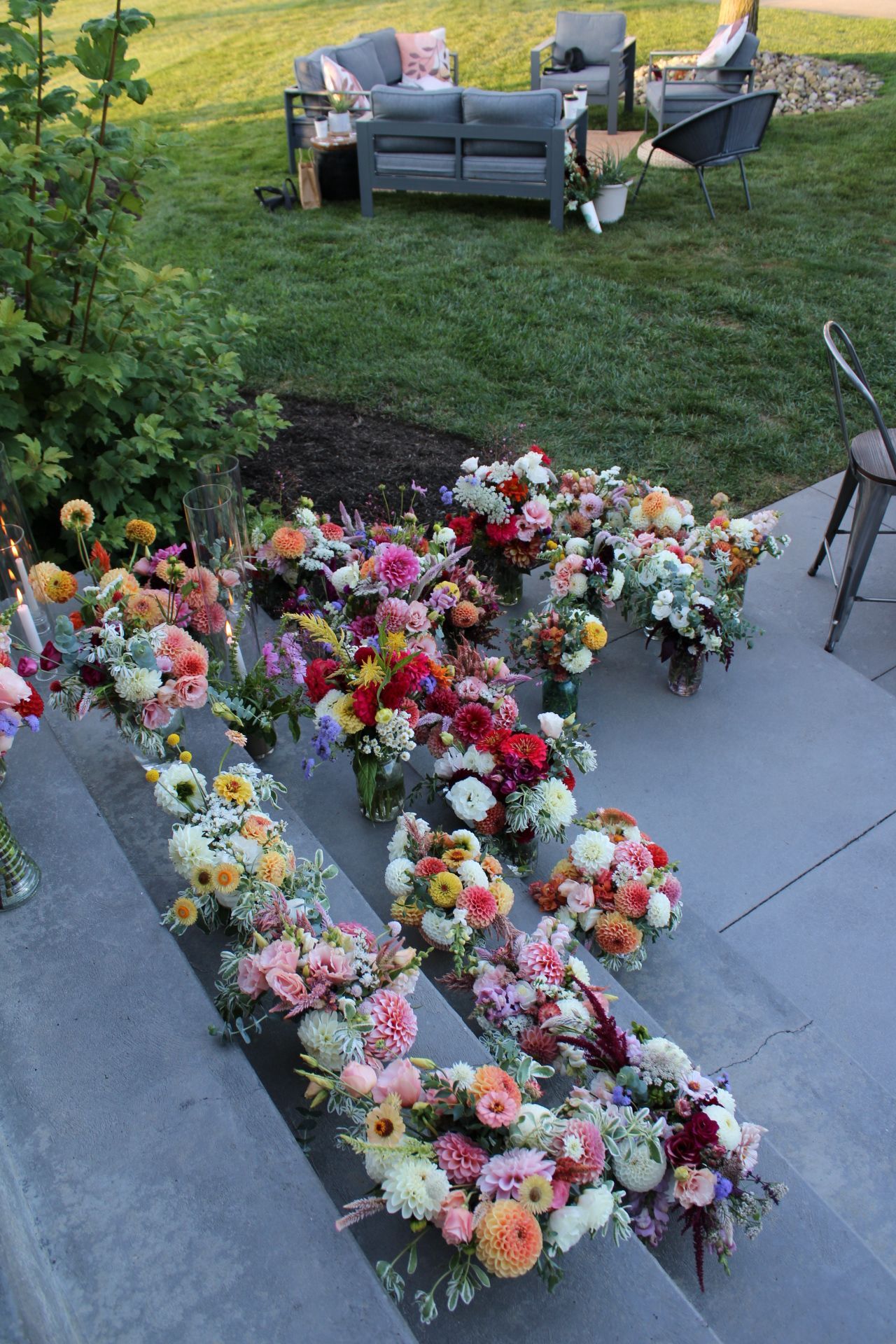 Colorful flower arrangements displayed on a concrete patio with outdoor furniture in the background.