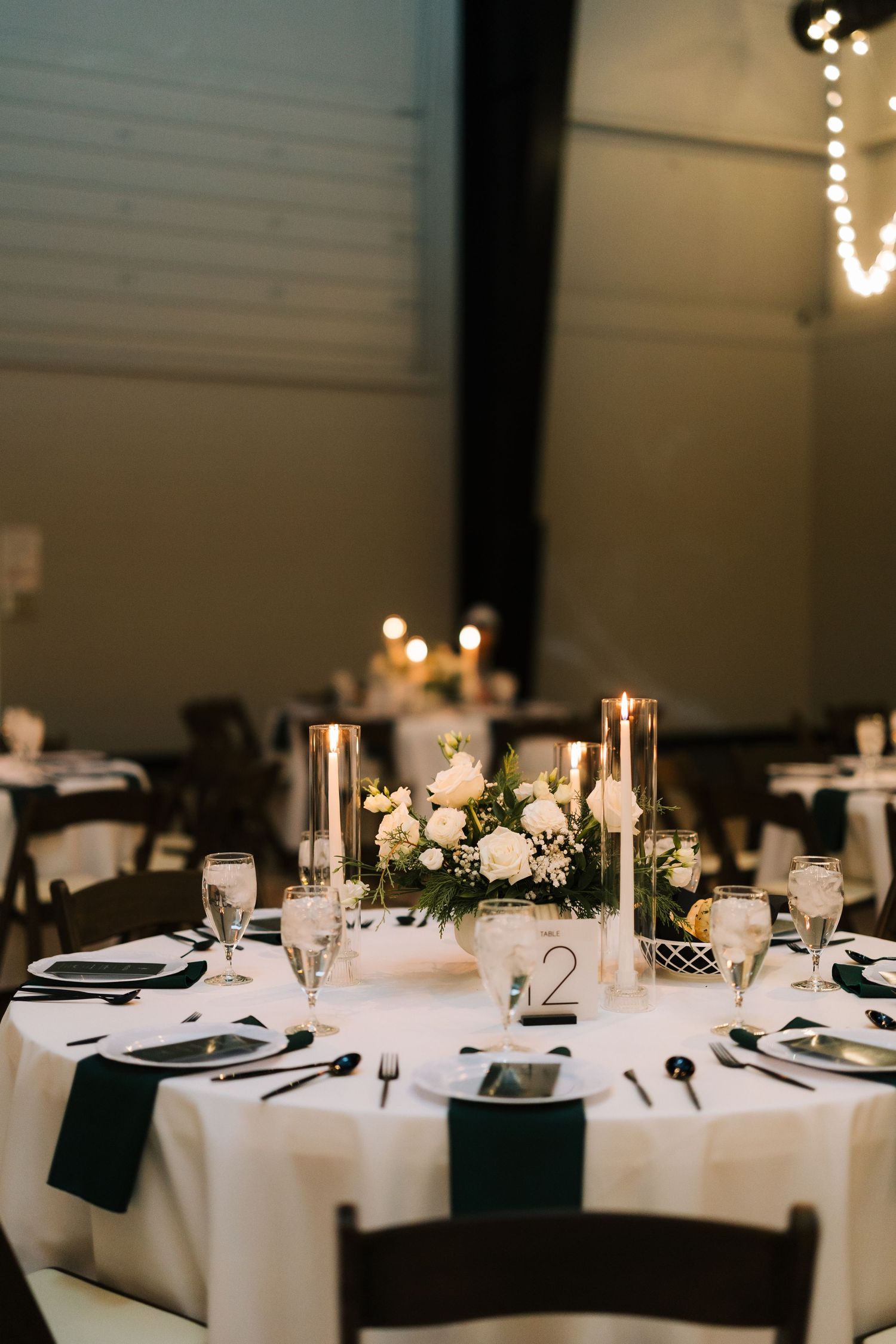 Elegant wedding reception tables with white linens, black napkins, and romantic candlelight create an intimate dining atmosphere.