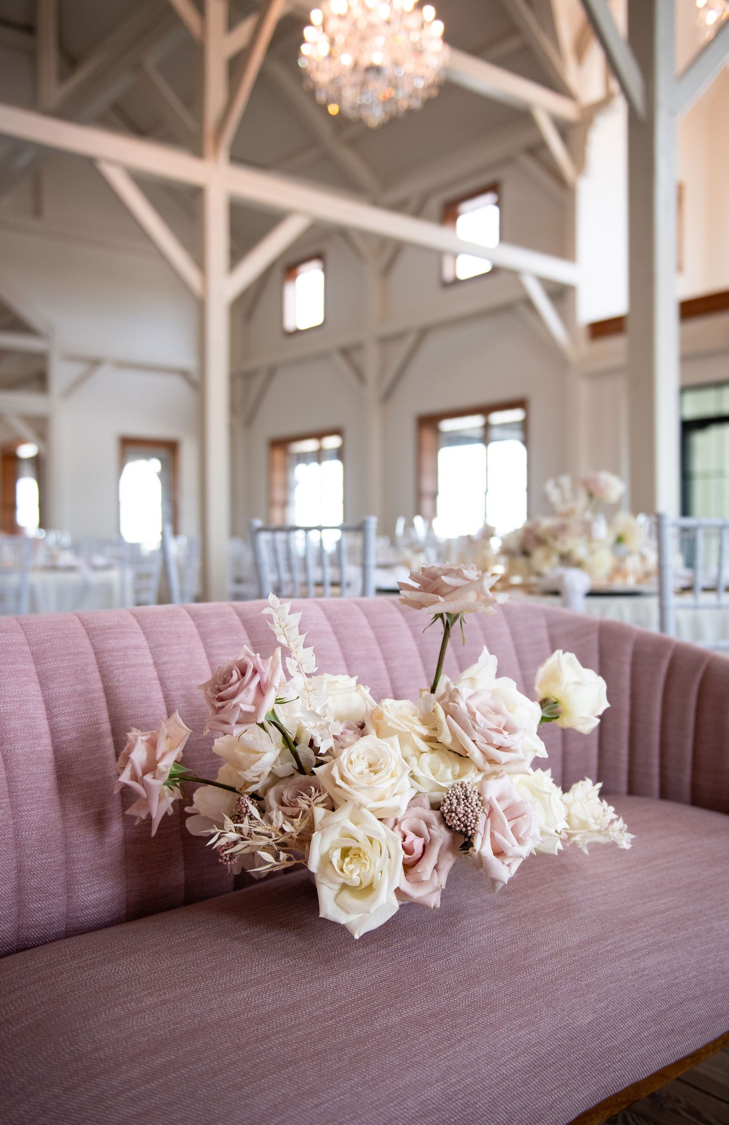 Pink velvet seating with delicate pink and white rose arrangement in an elegant white venue.