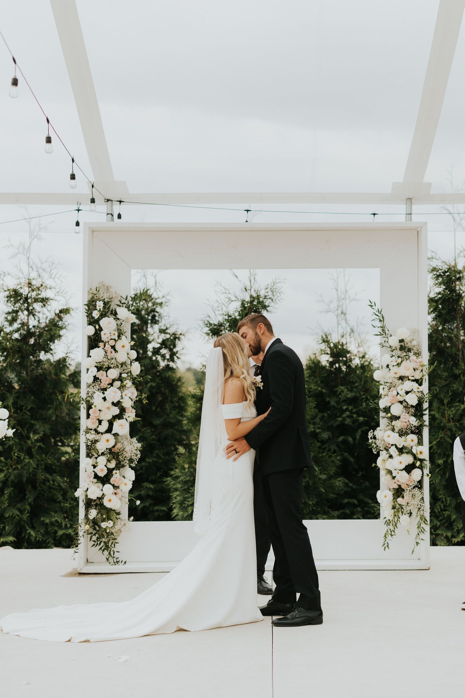 Elegant white wedding pavilion decorated with floral columns and string lights for outdoor ceremony.