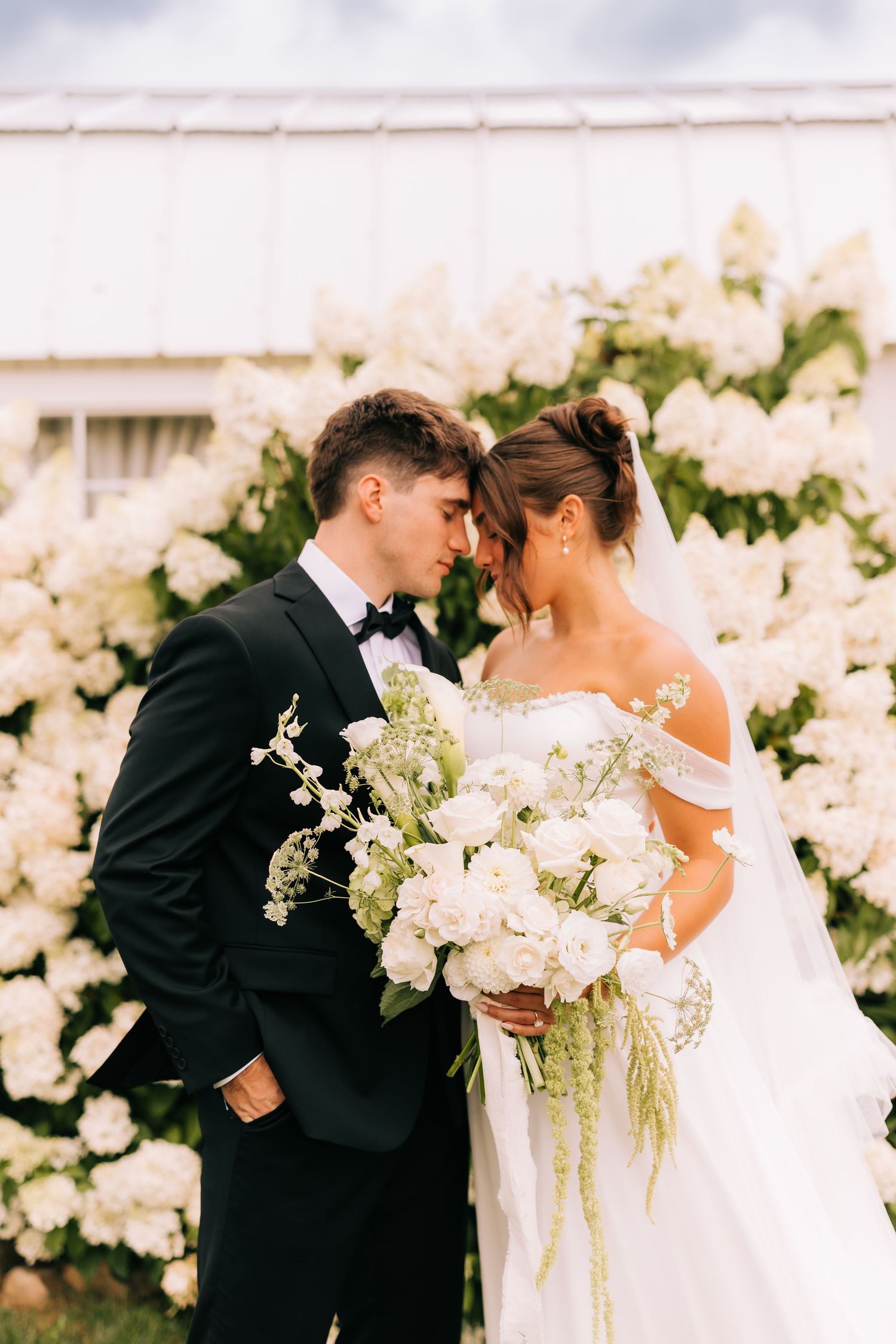Elegant wedding scene with white floral arrangements and romantic moment against soft neutral background.